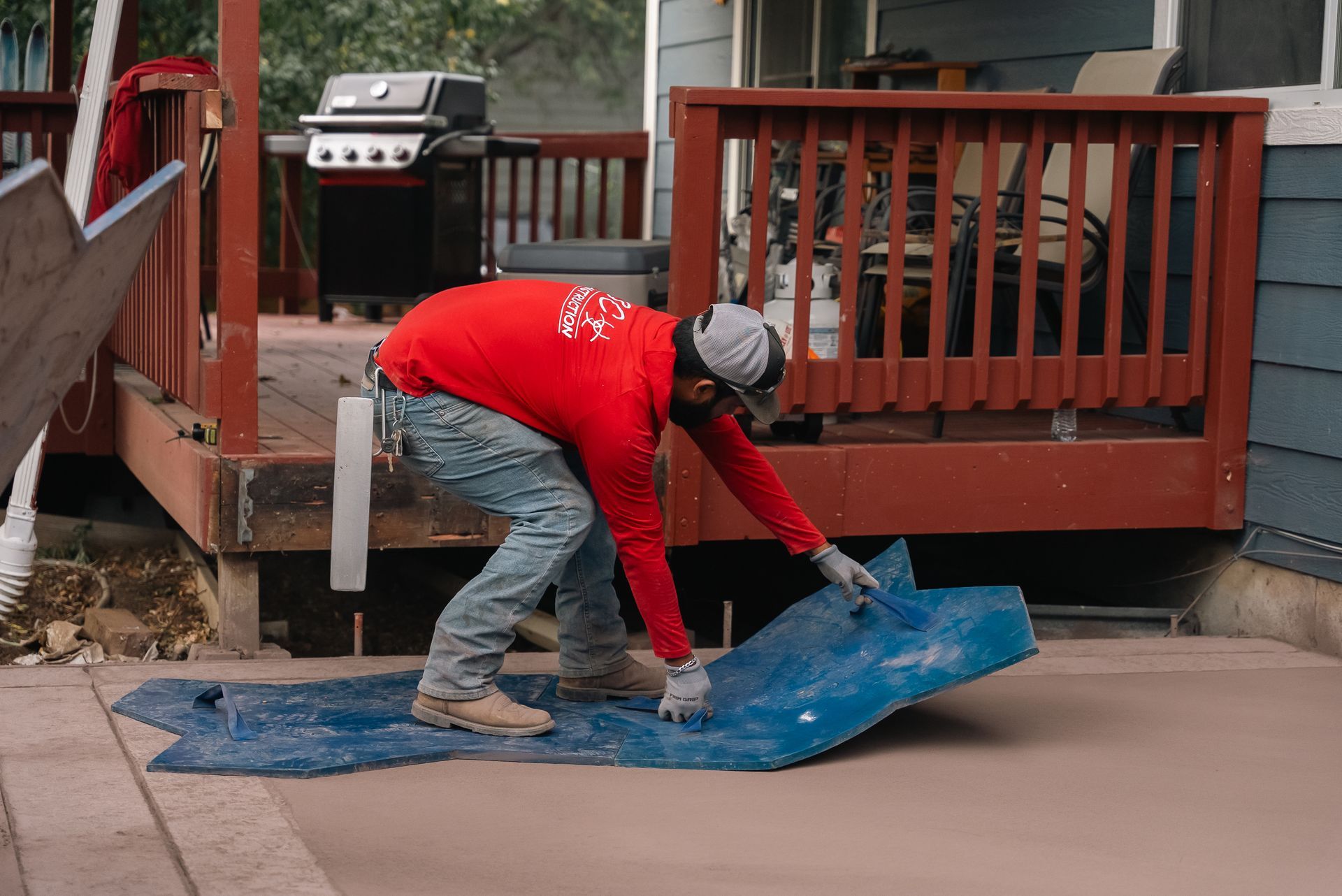 Construction worker placing blue material on concrete patio next to wooden deck.