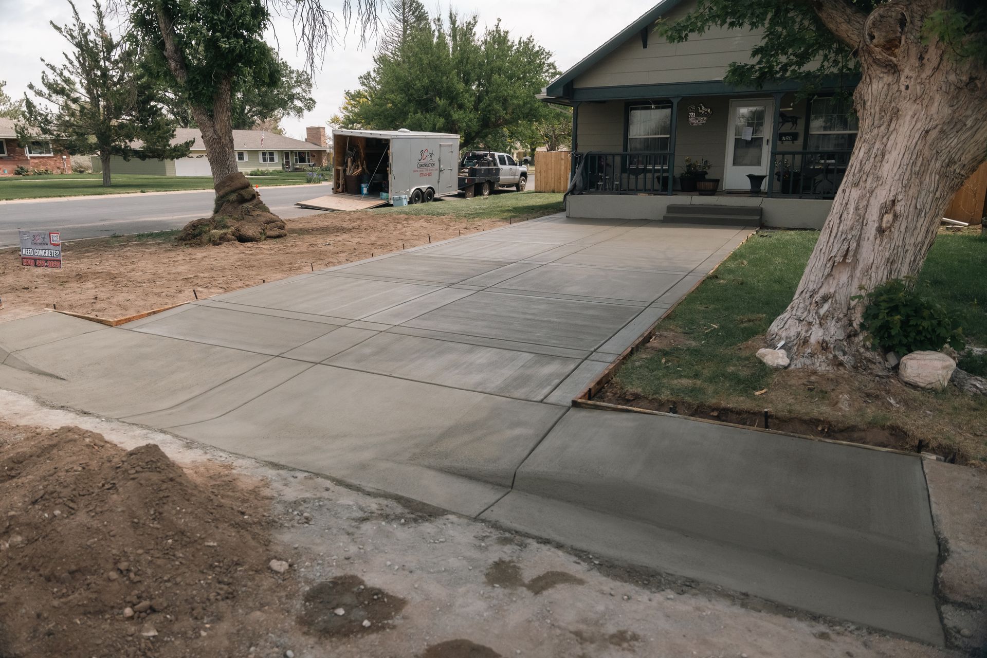 Concrete driveway and sidewalk freshly poured in front of a house, construction materials visible.
