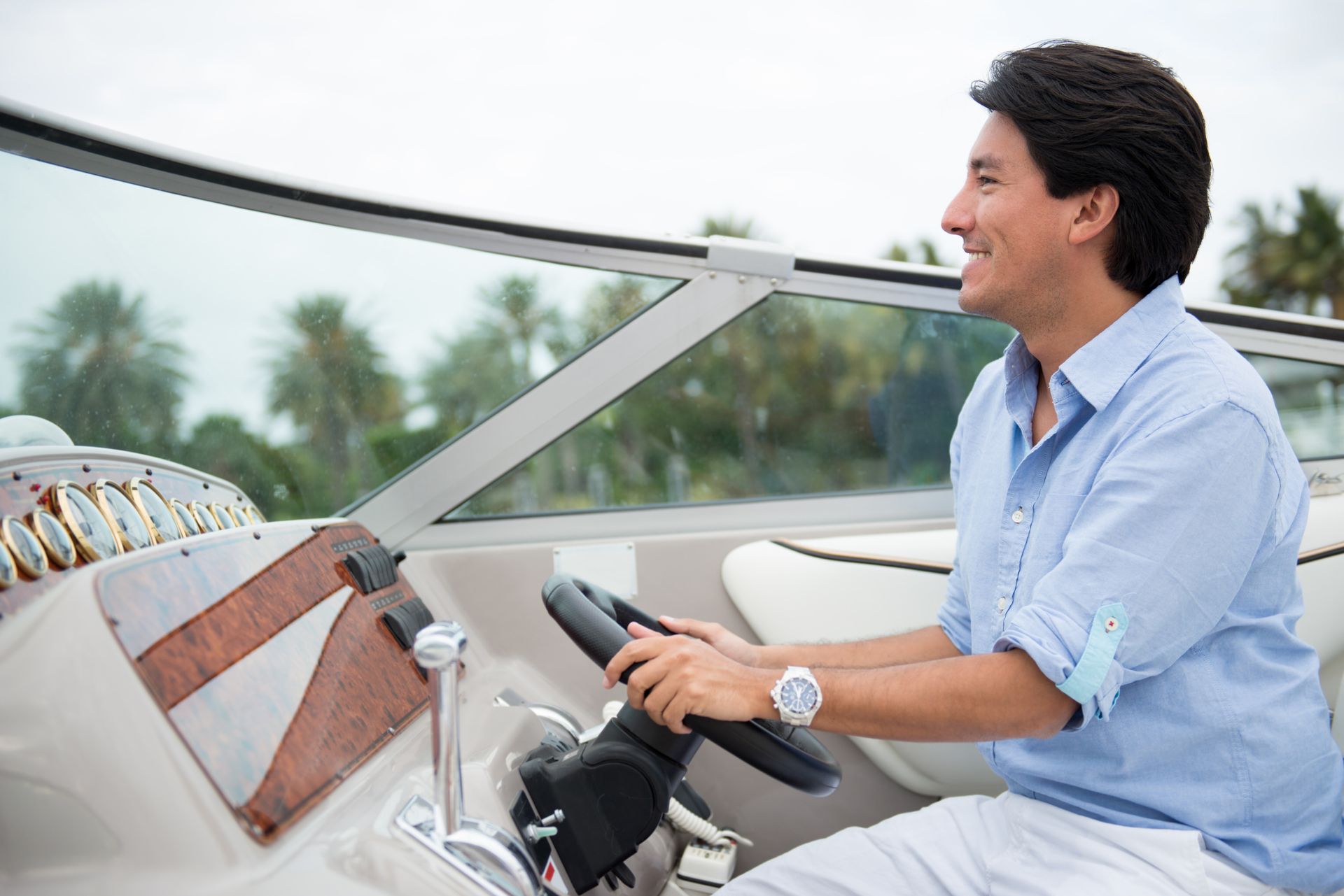 Man smiling while steering a motorboat on a cloudy day.