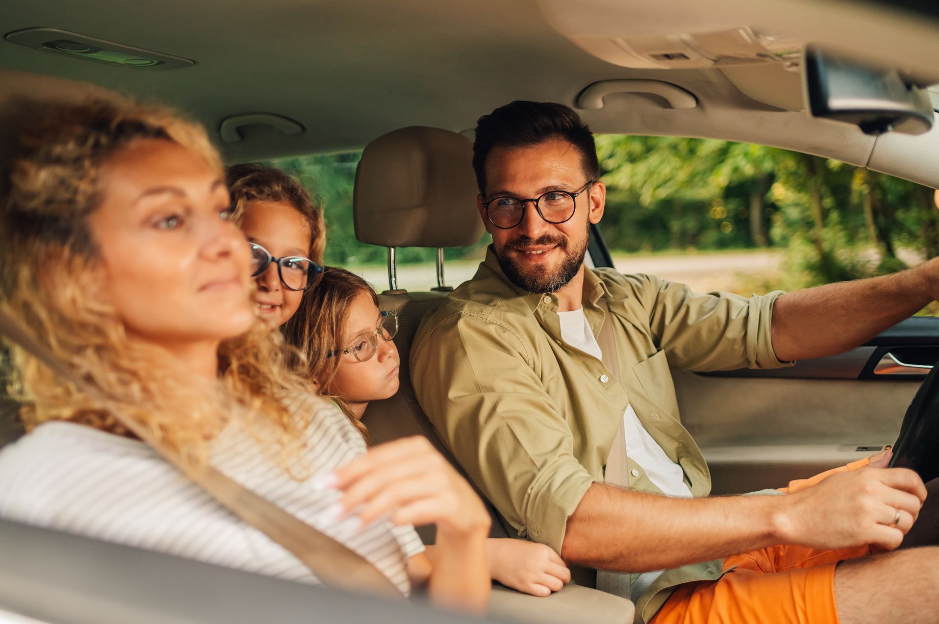 Family in car; father driving, mother and children in back seat, smiling.