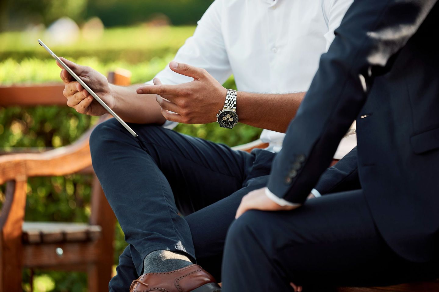 Two men are sitting on a bench looking at a tablet.