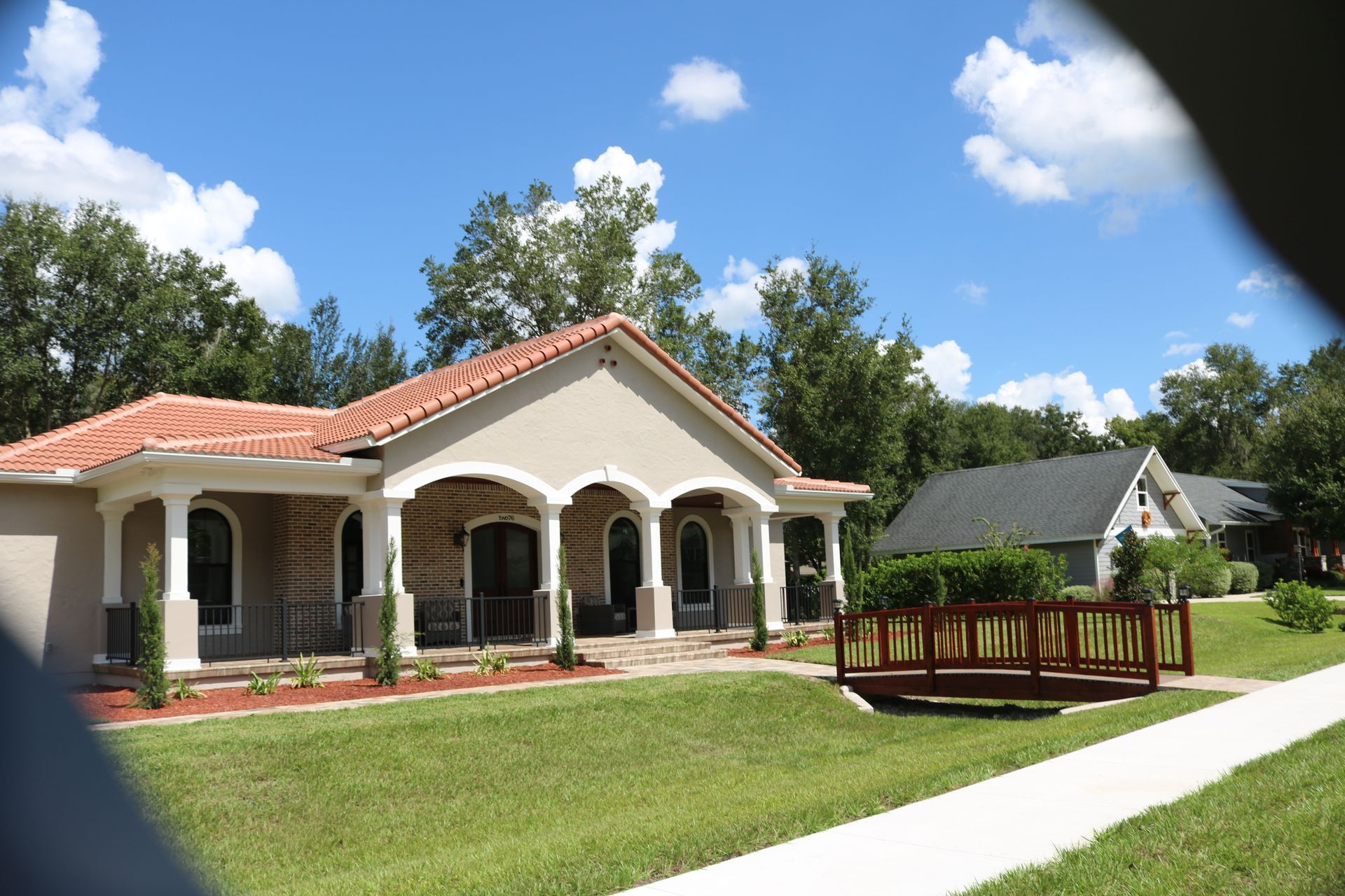 A light-colored house with a red tile roof and a small wooden bridge on a sunny day.