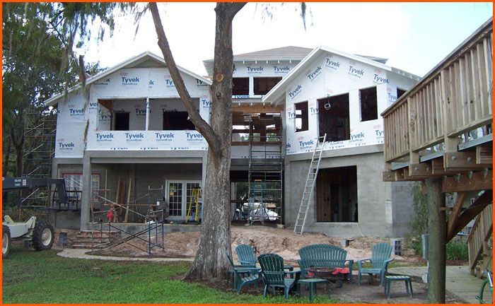 House under construction, covered in Tyvek, with a ladder and outdoor seating in front.