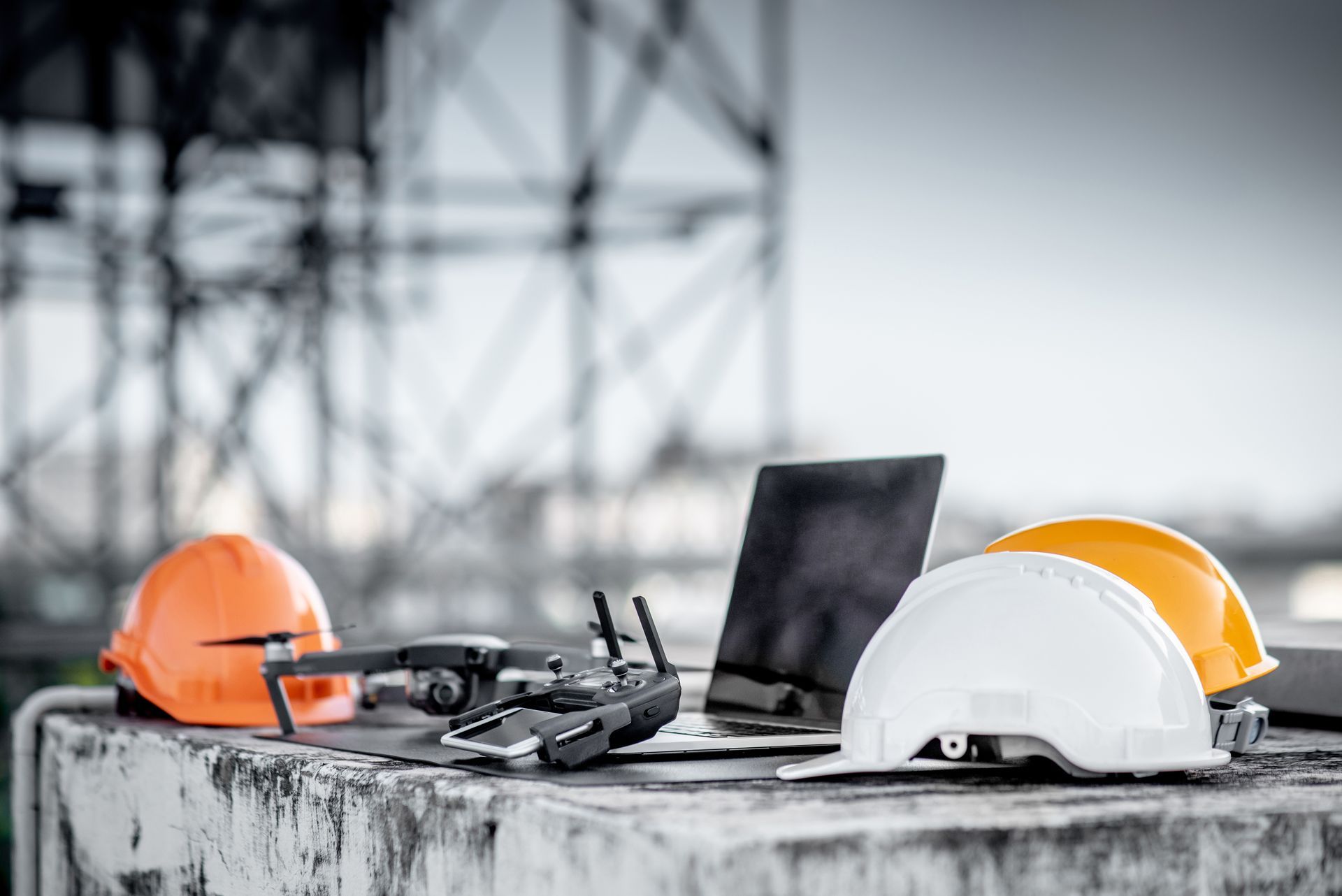 Drone, laptop, and safety helmets on a concrete surface with blurred industrial background.