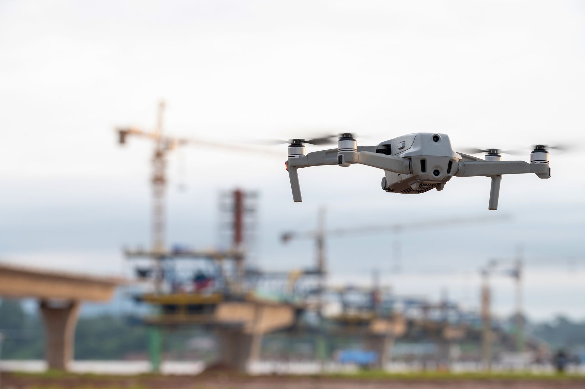 Drone flying over a construction site with cranes and bridge in the background.
