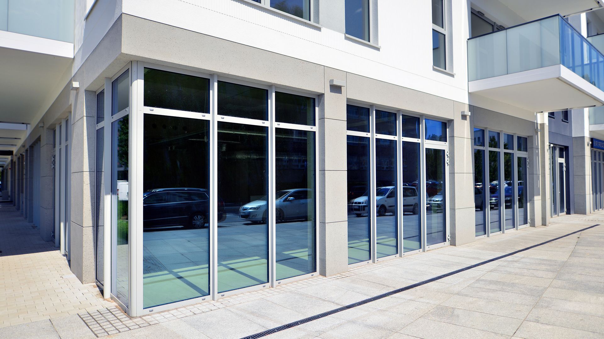 Storefront with large glass windows reflecting cars, beneath a white building.