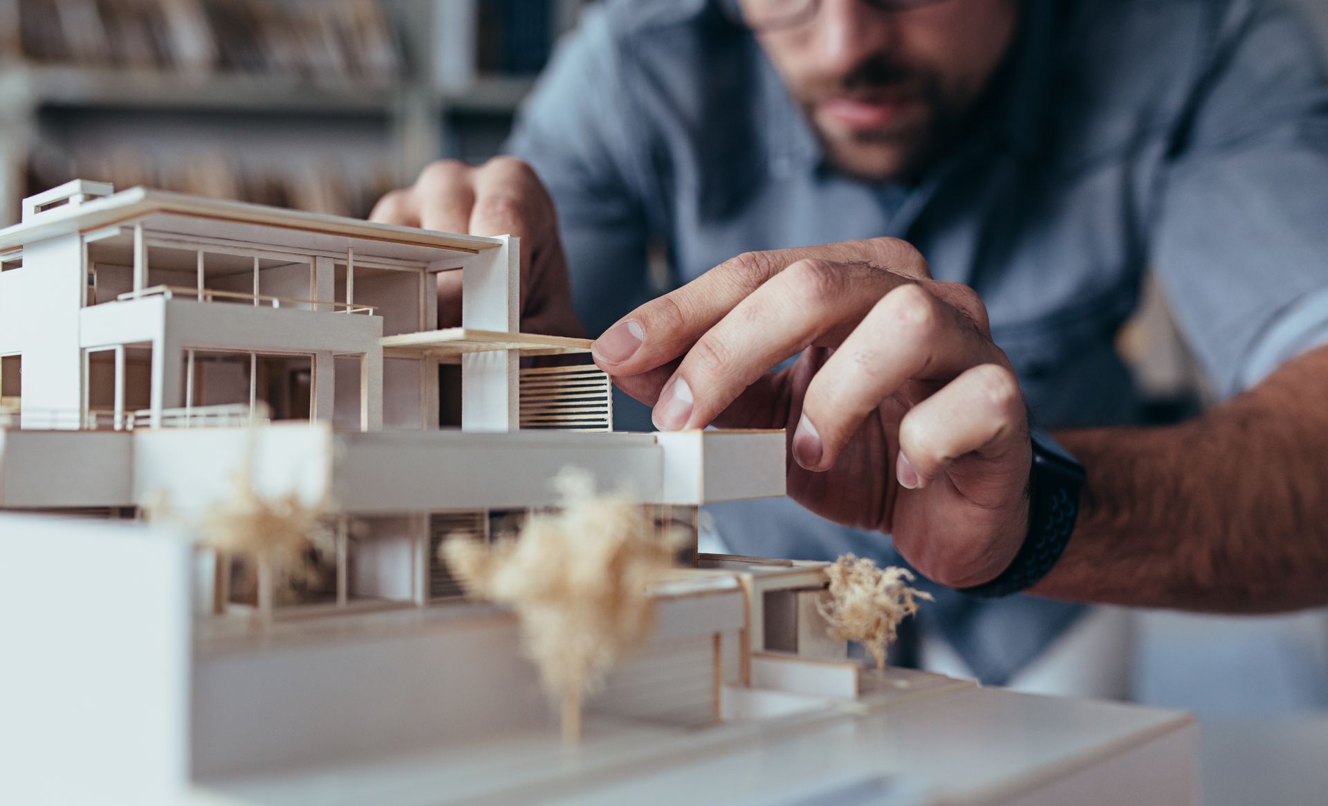 Architect building a model house; hands working on rooftop detail; white model in focus.