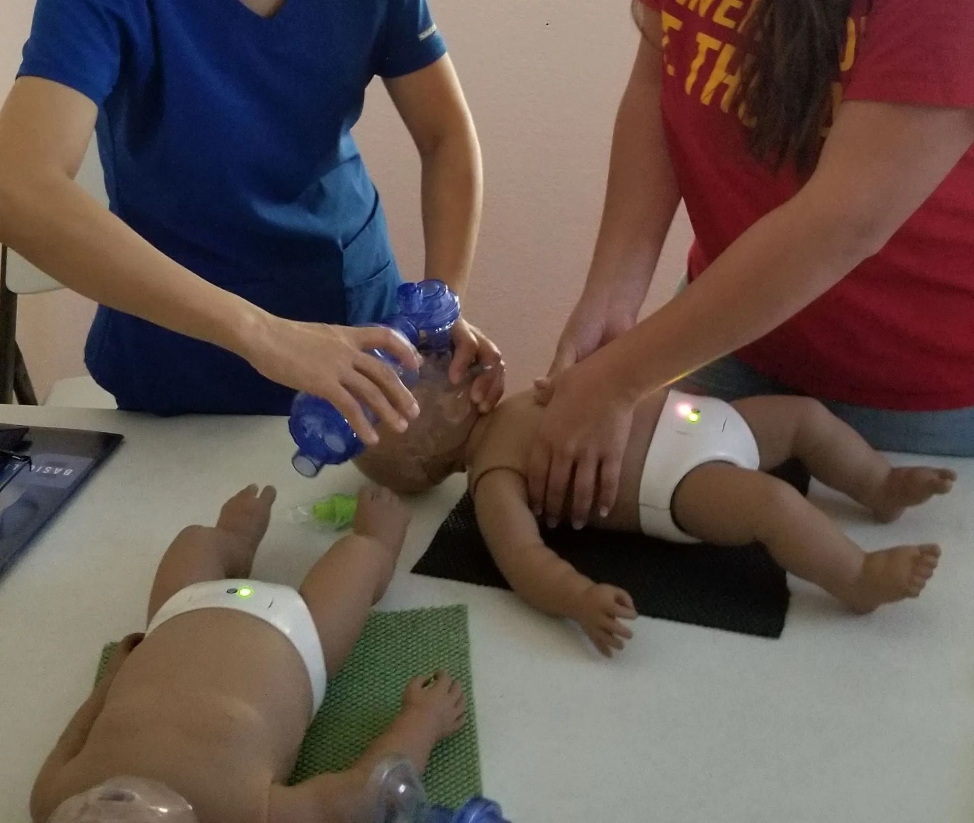 Two people practicing infant CPR on training mannequins.