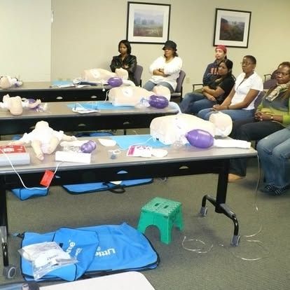 People in a classroom setting attending a CPR training. Mannequins on tables.