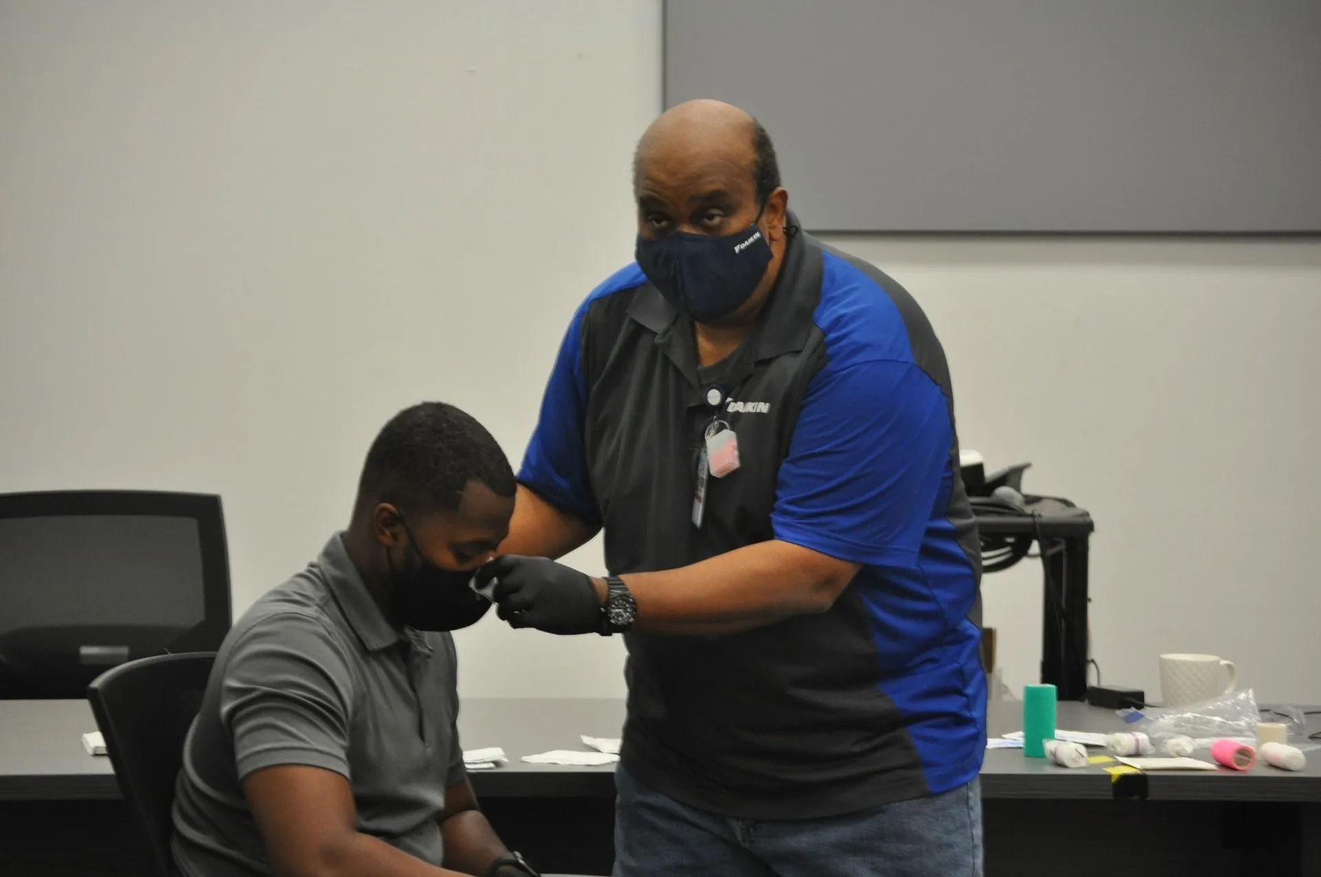 Man wearing a mask and gloves administers a nasal swab to another man in a room with medical supplies.