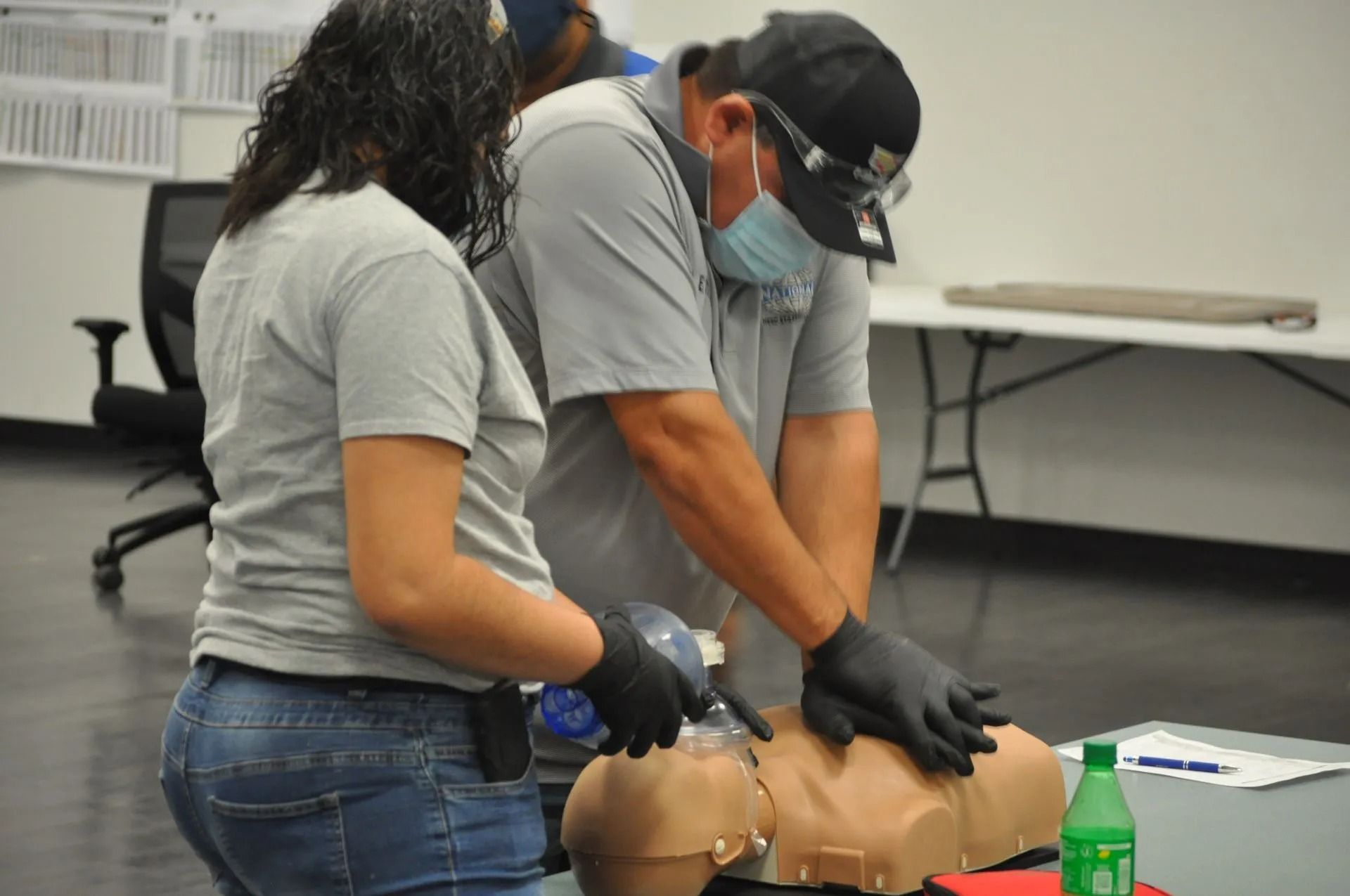Man wearing a mask and gloves administers a nasal swab to another man in a room with medical supplies.