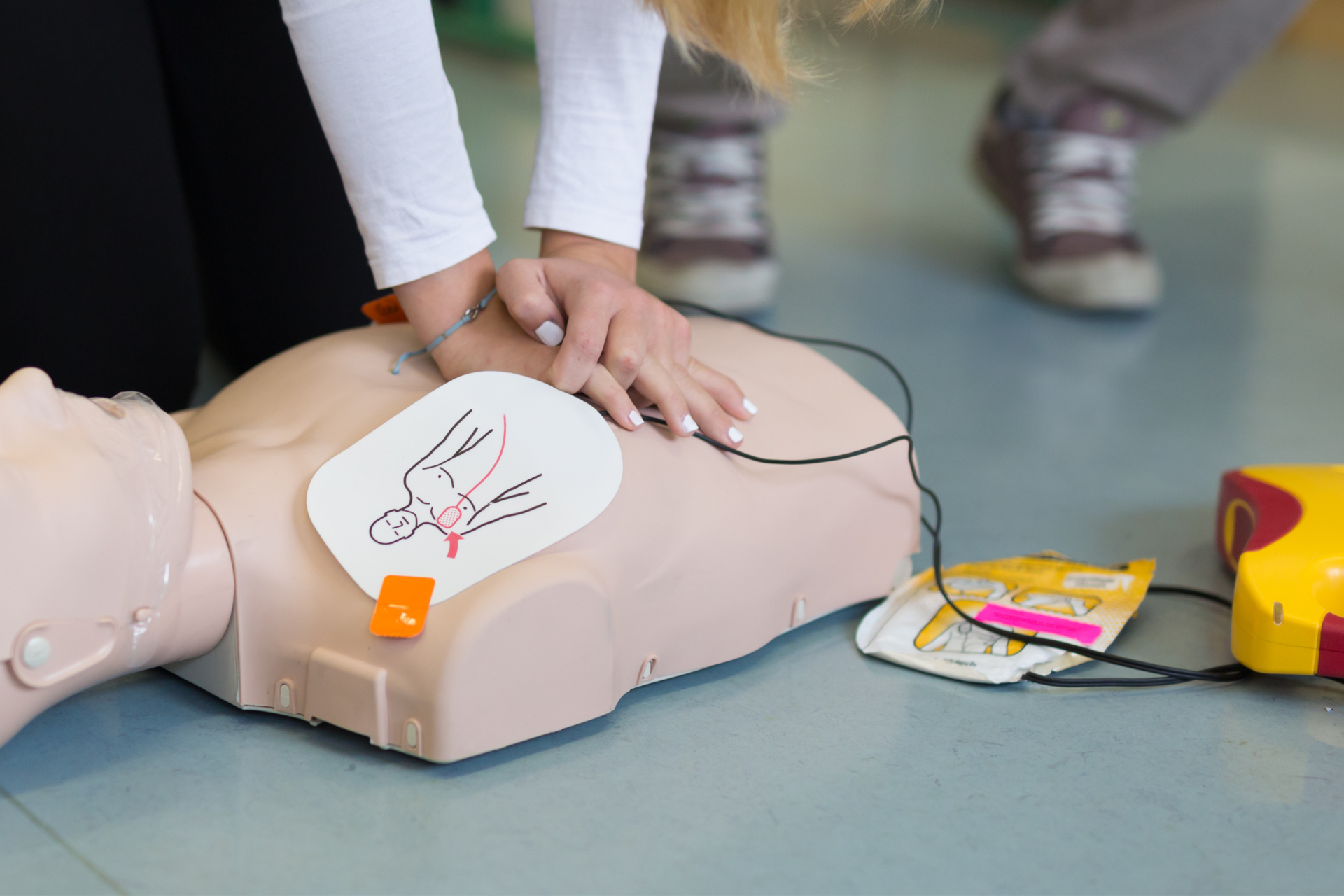 Person performing CPR on a mannequin, with defibrillator pads attached.