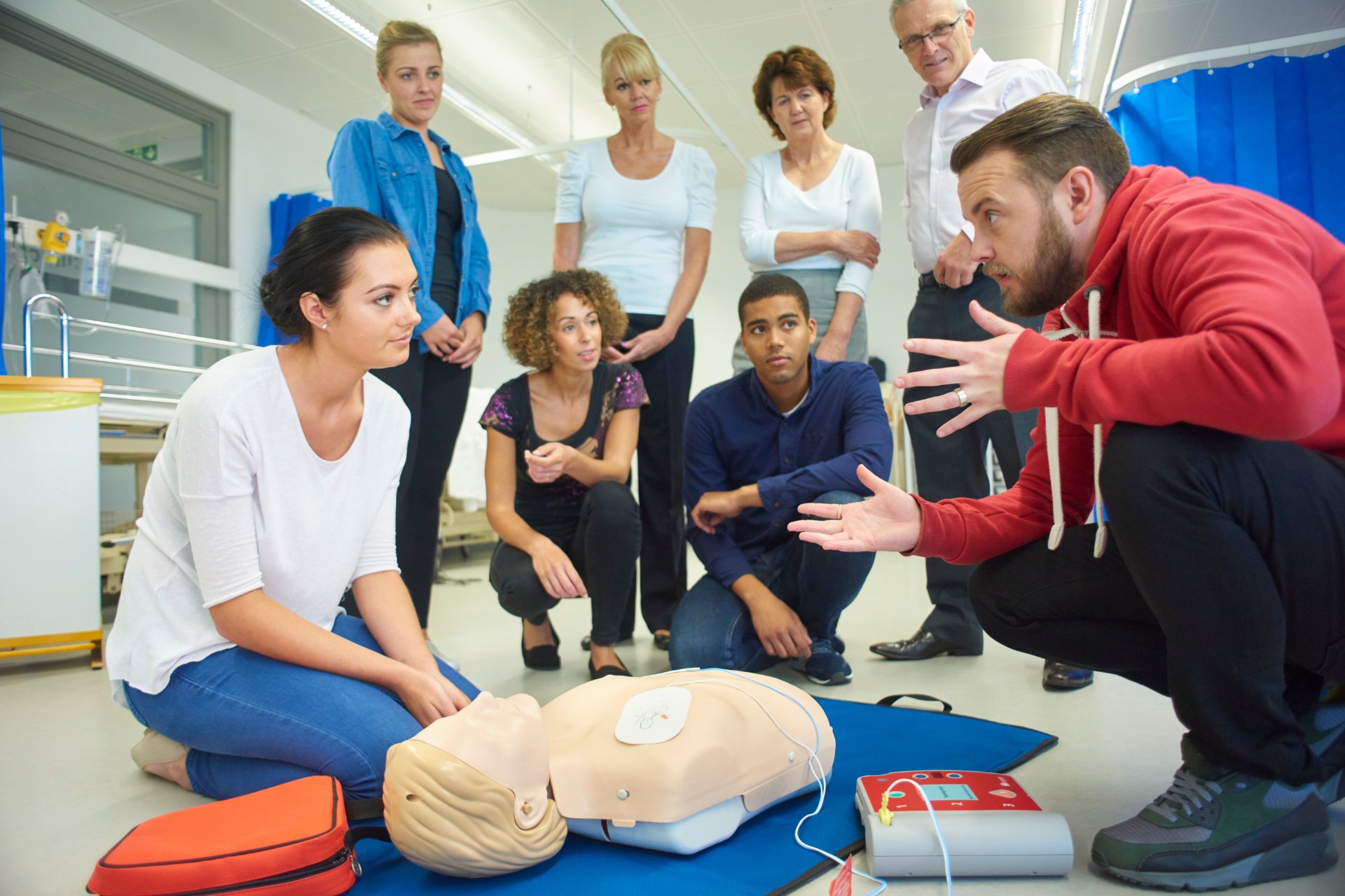 CPR training: Instructor demonstrating technique on a mannequin, surrounded by attentive participants in a medical setting.