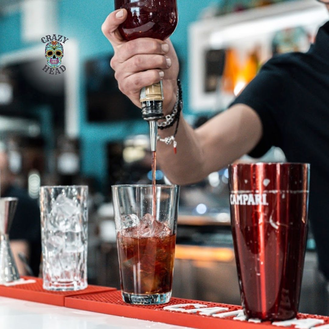 Un barista versa un drink in un bicchiere su cui c'è scritto campari