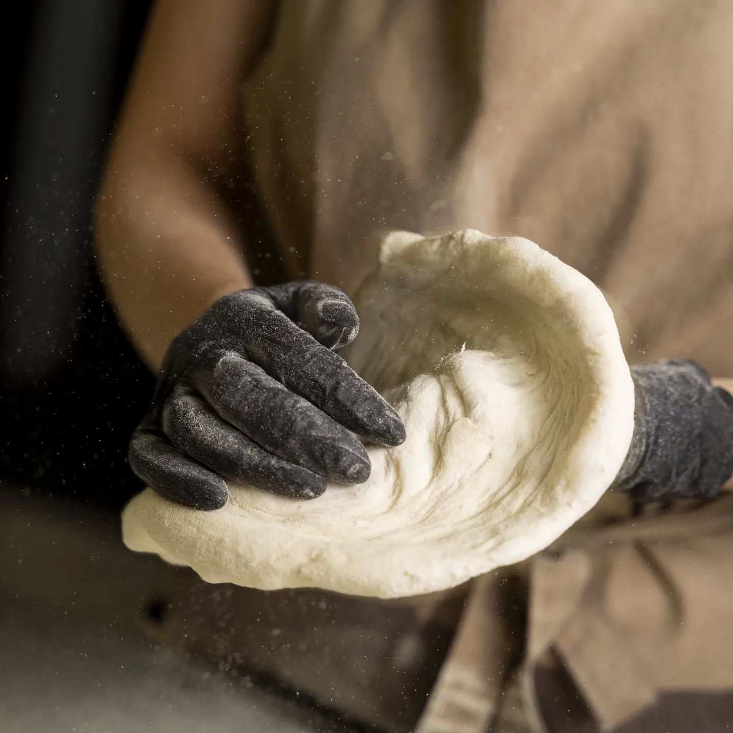 Una persona che indossa guanti neri tiene in mano un pezzo di pasta.