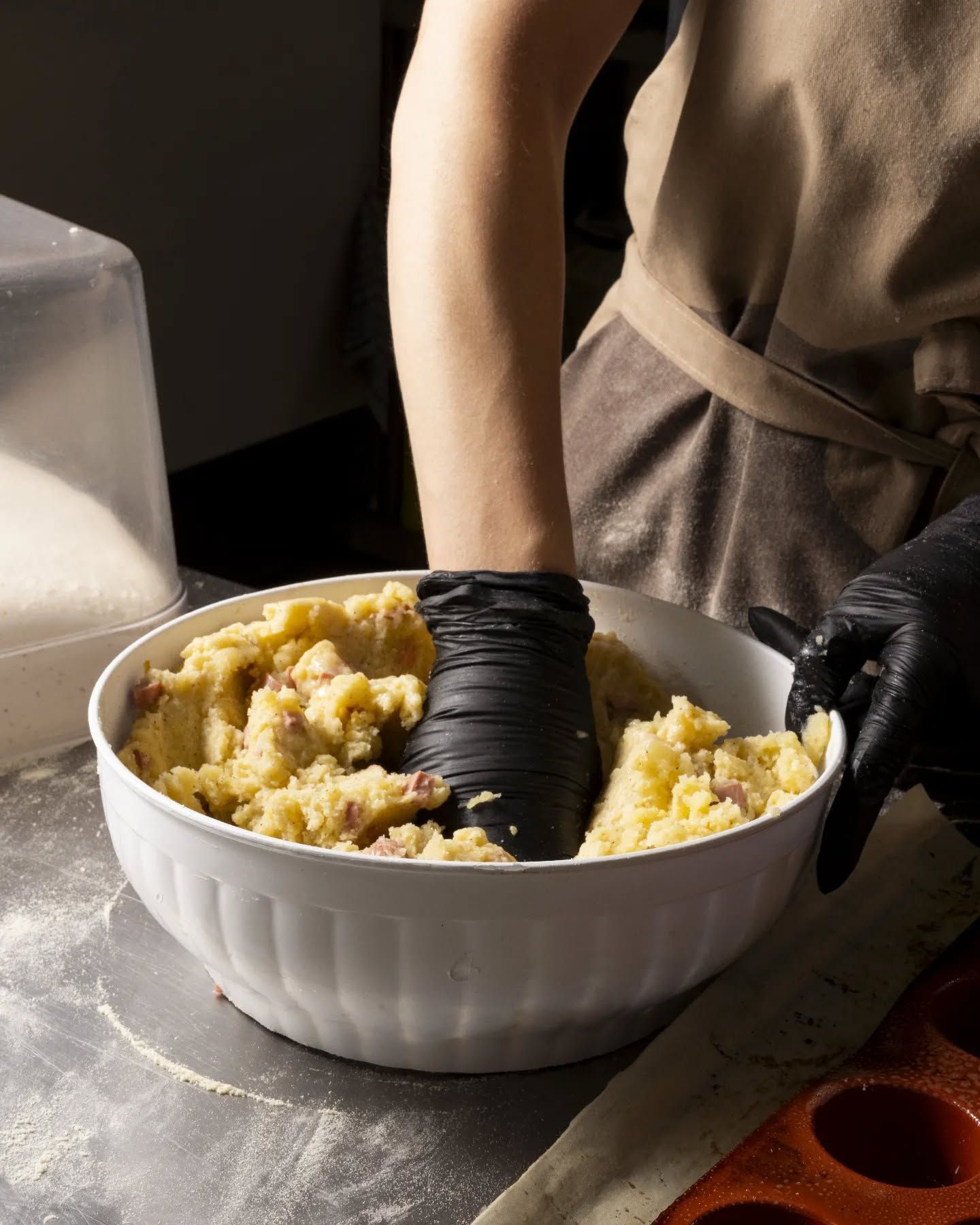 Una persona che indossa guanti neri sta impastando in una ciotola bianca.