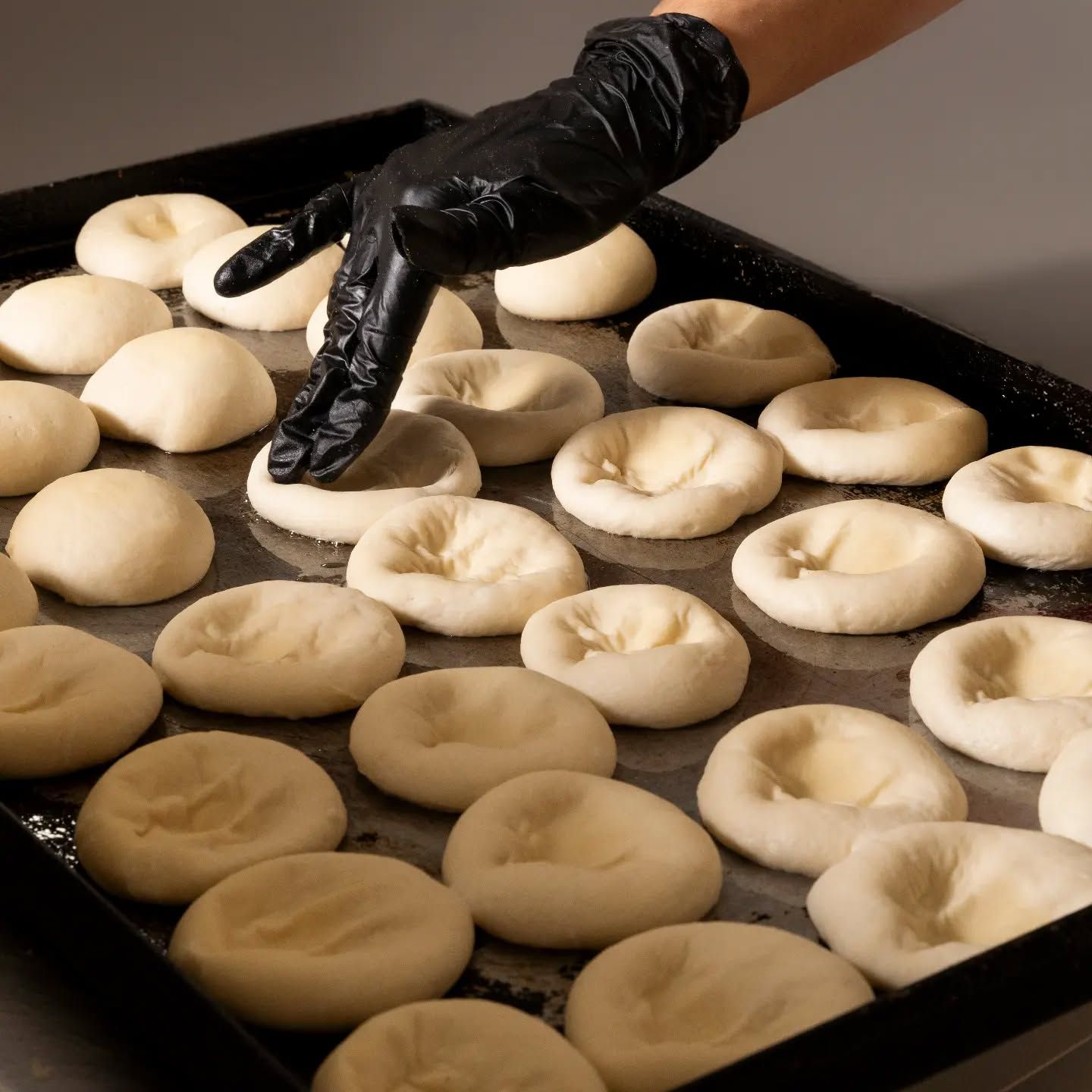 Una persona che indossa guanti neri sta infilando la mano in un vassoio di pasta