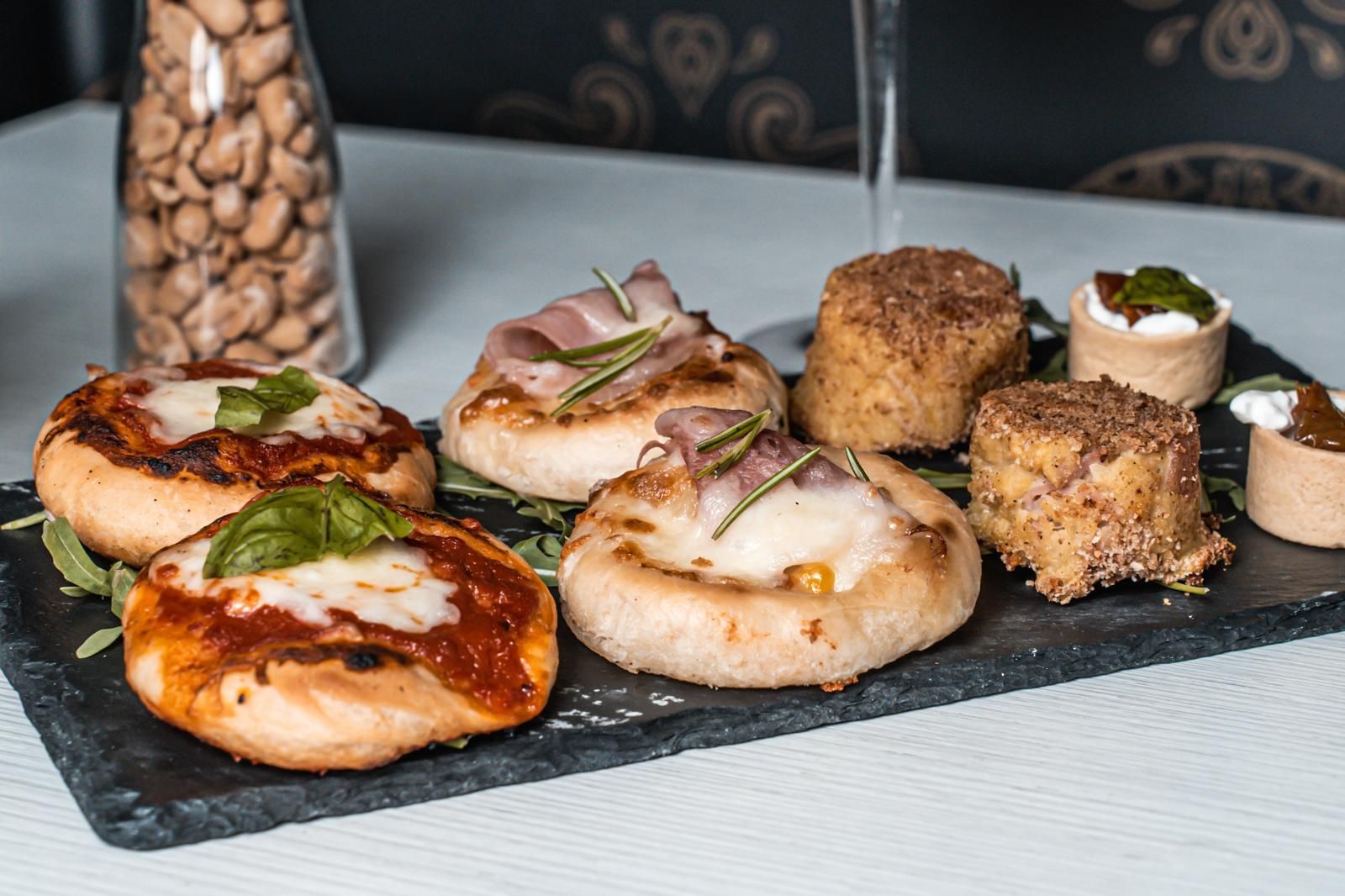 Una varietà di pizze e pasticcini sono disposti su un vassoio di ardesia su un tavolo.