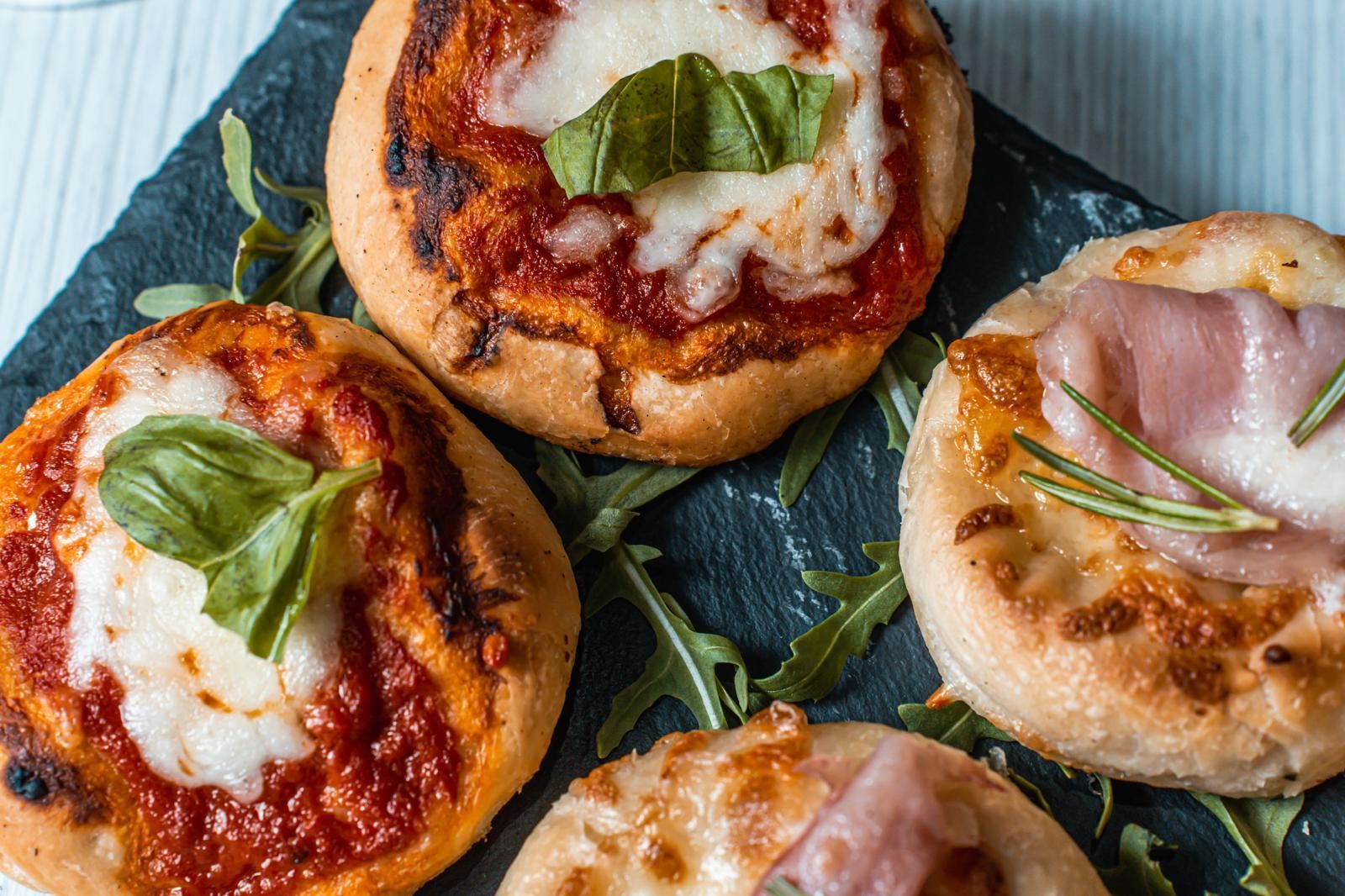 Quattro mini pizze con condimenti diversi su una teglia di ardesia.