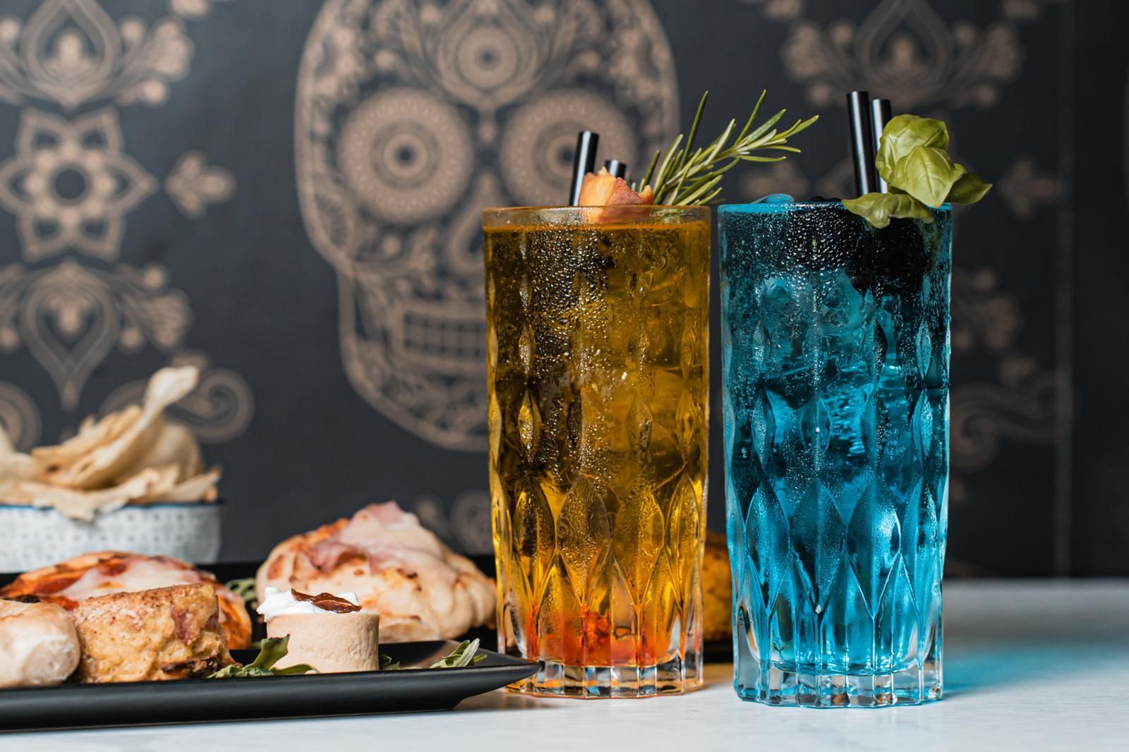 Due drink sono appoggiati su un tavolo accanto a un piatto di cibo.