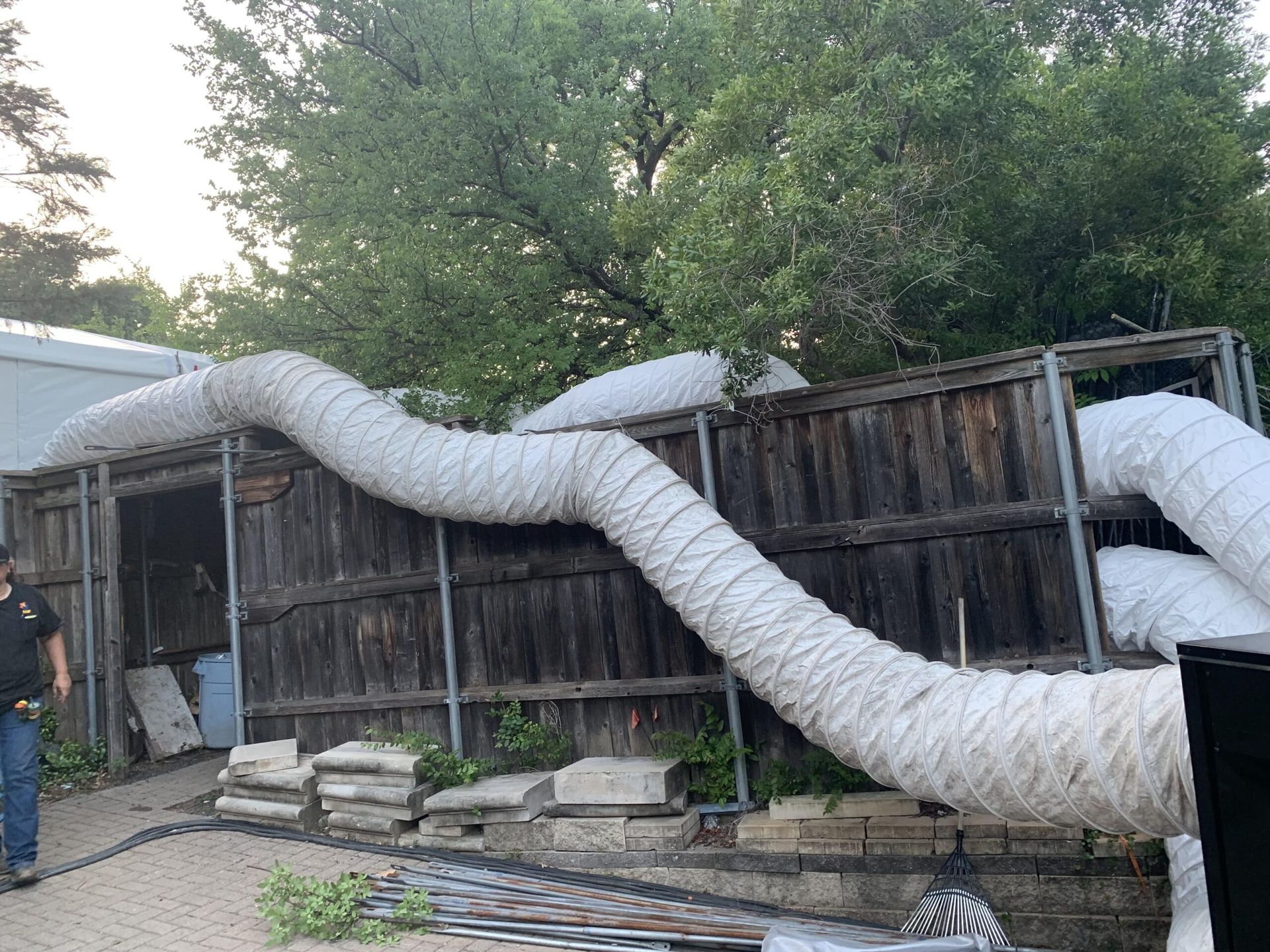 A man is standing in front of a wooden fence with a hose attached to it.