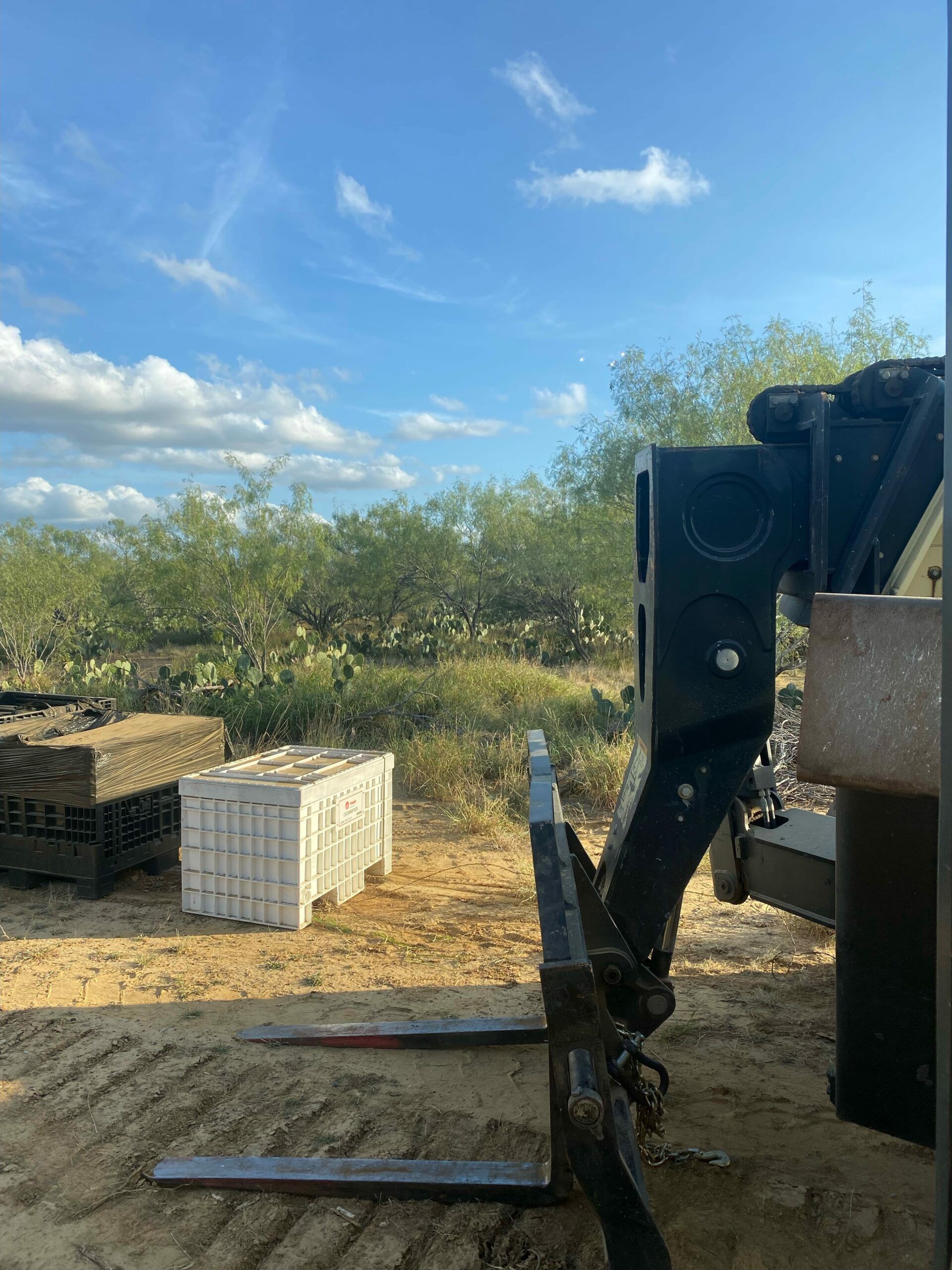 A forklift is sitting in the dirt next to a truck.