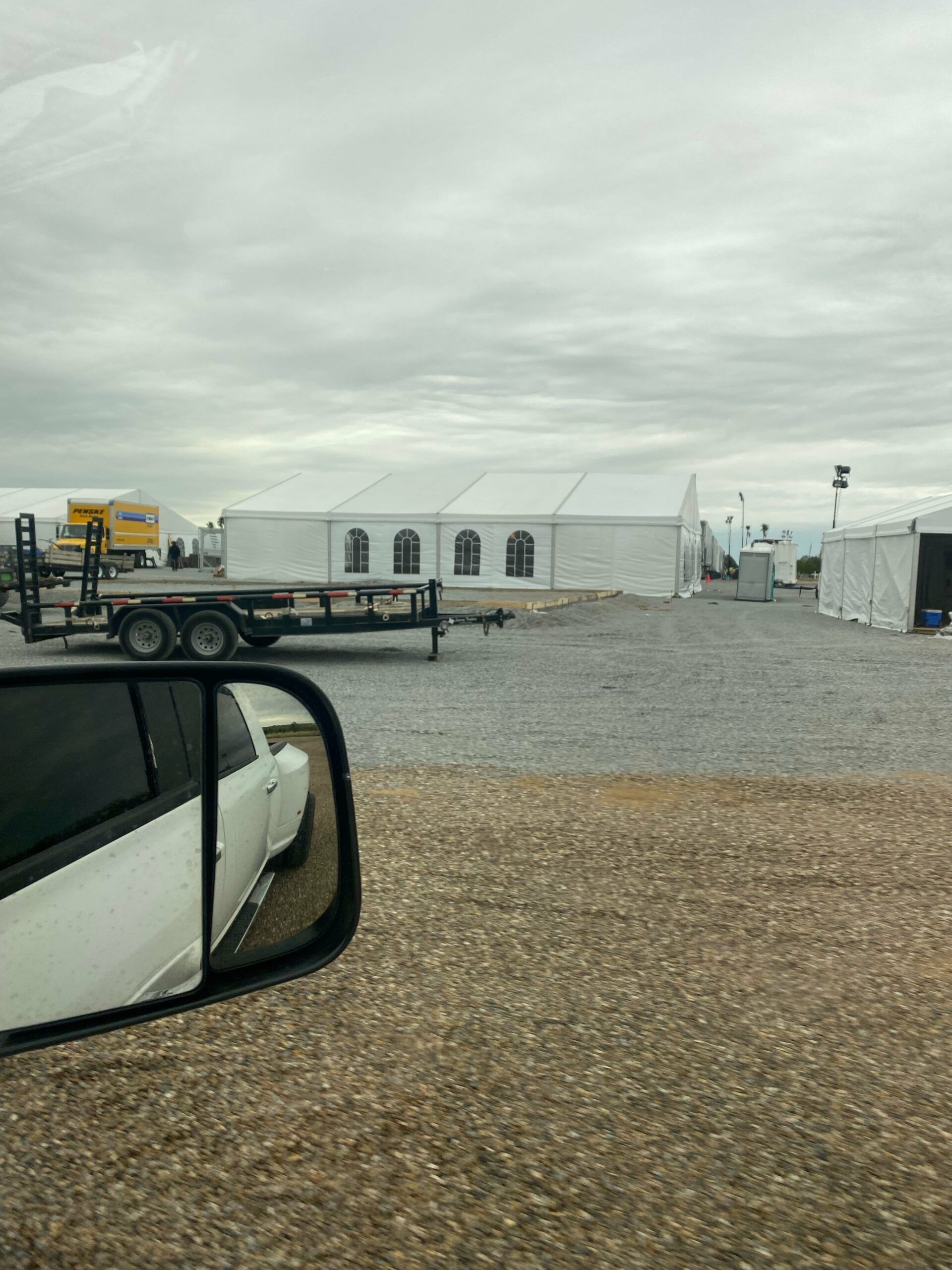 A car is parked in a gravel lot next to a trailer.
