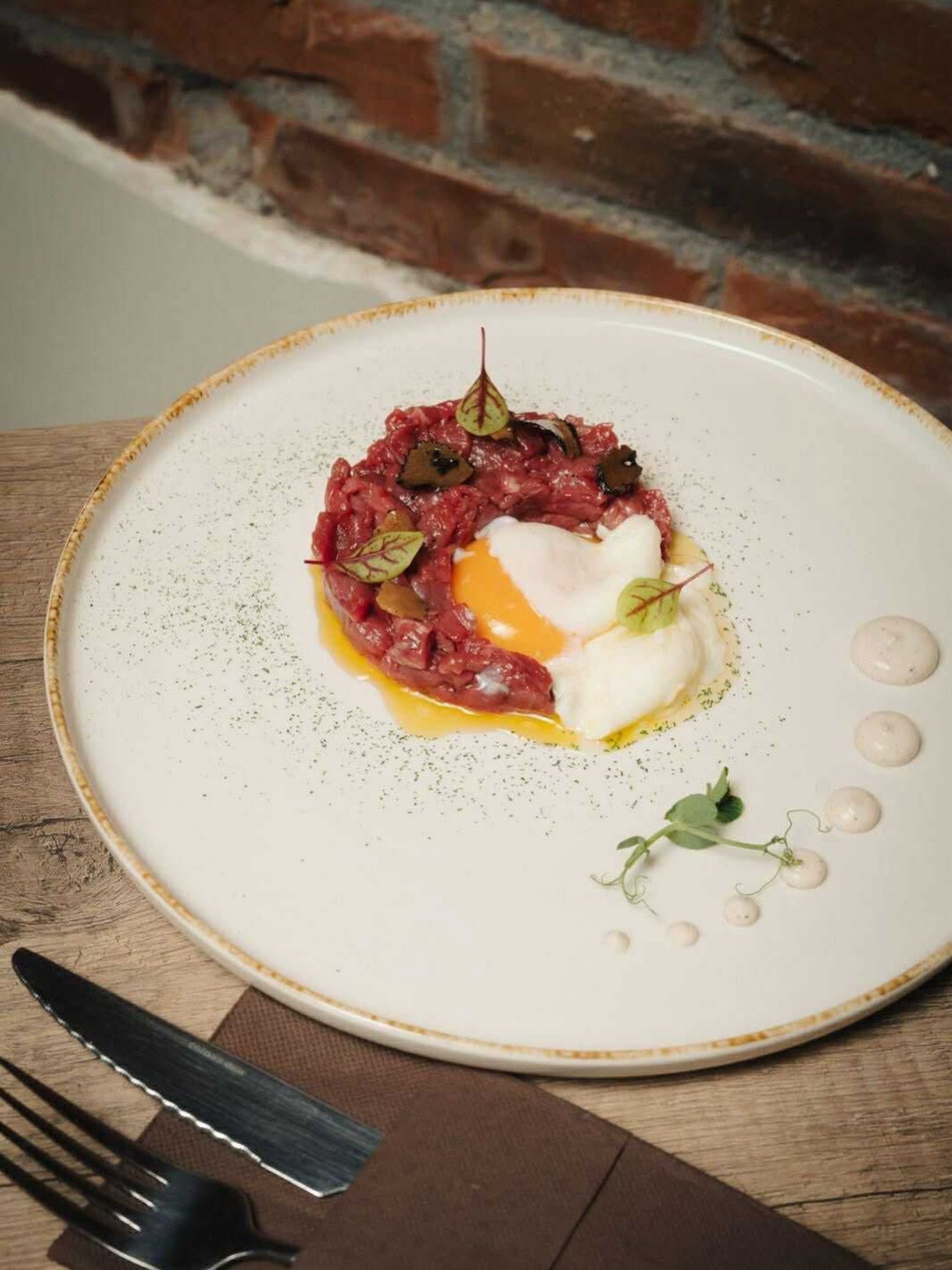 Piatto gourmet impiattato con guarnizione rossa e salsa bianca su un piatto bianco accanto alle posate su un tavolo