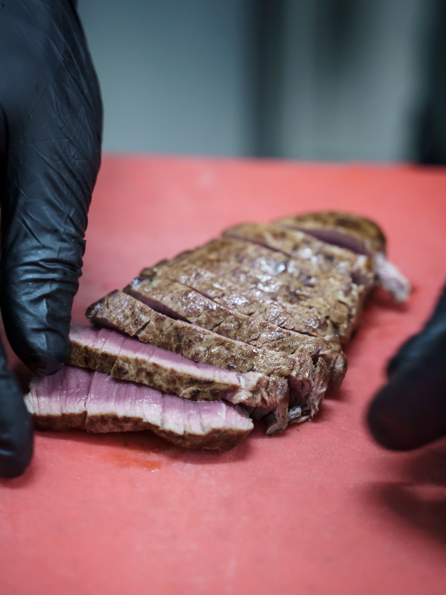 Mani guantate che affettano una bistecca scottata su un tagliere rosso