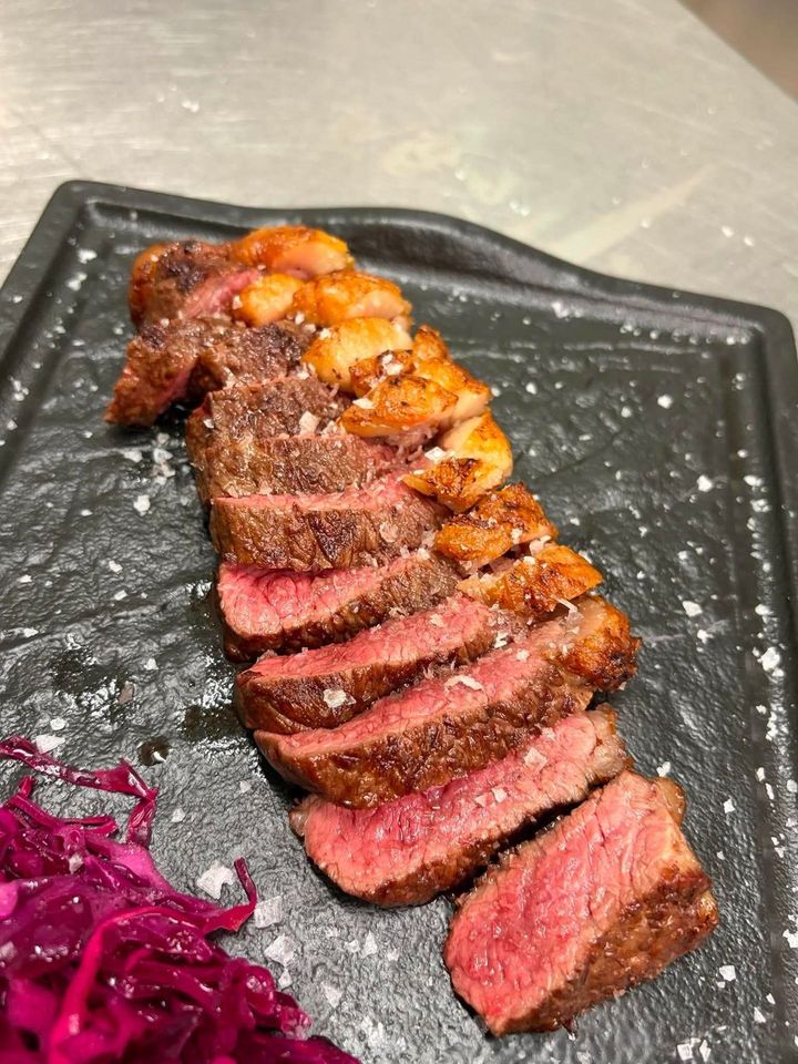 Fettine di bistecca scottate in padella con patate arrosto su un piatto nero, accompagnate da cavolo rosso.