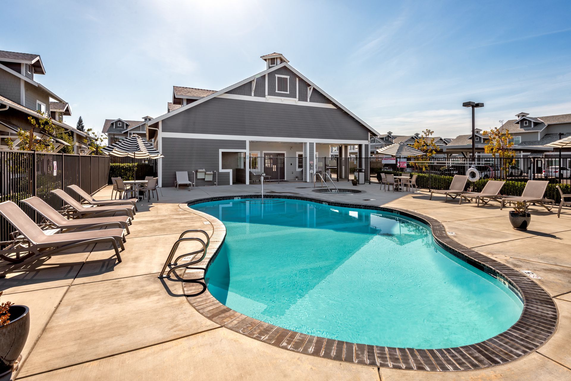 Pool with lounge chairs and a gray building on a sunny day.