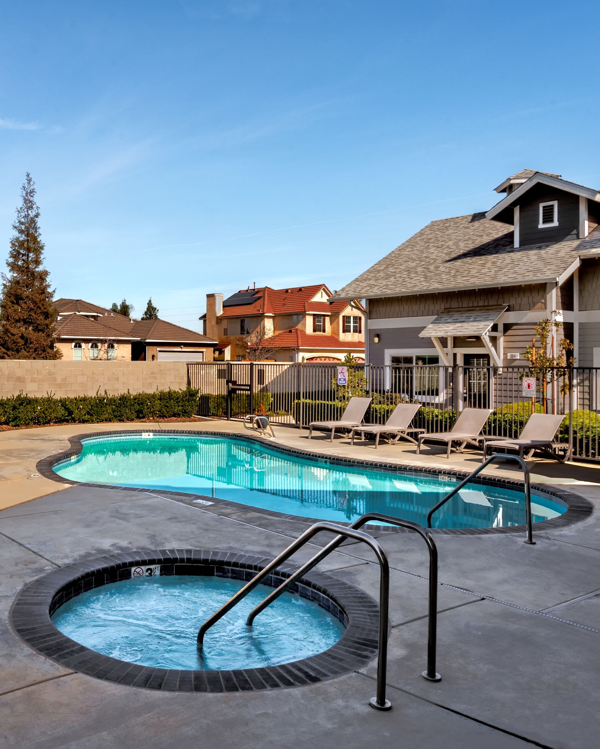 A pool and jacuzzi on a sunny day in front of an apartment building.
