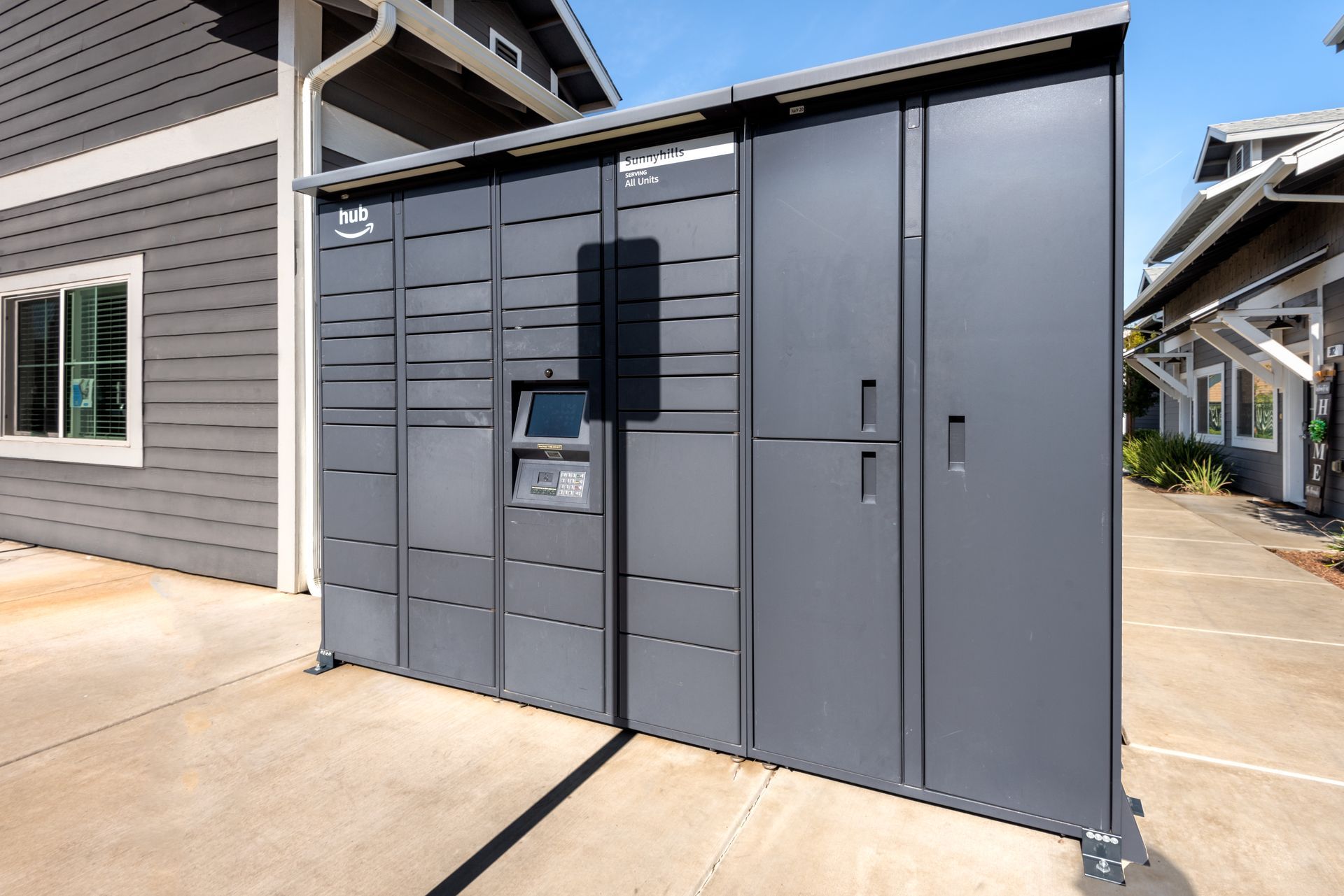 Dark gray package lockers near a building. A keypad and access panel are visible.