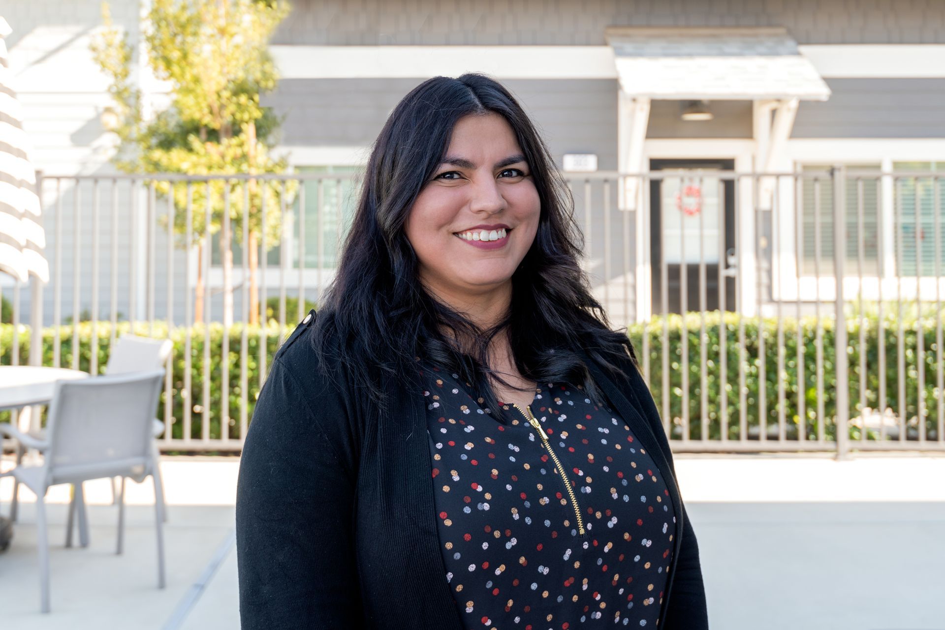Woman with dark hair smiles outside, wearing a patterned shirt and black cardigan.