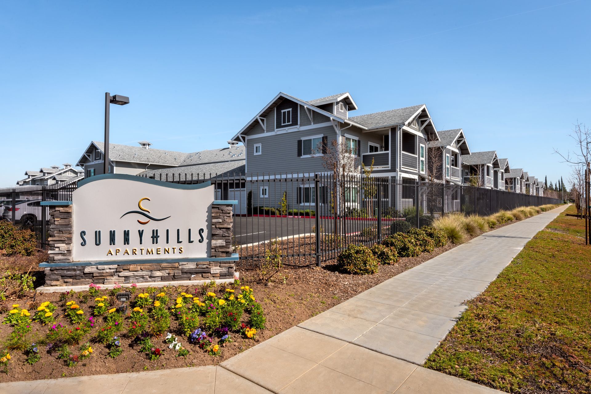 Sunny Hills Apartments sign with gray buildings and landscaping in front.