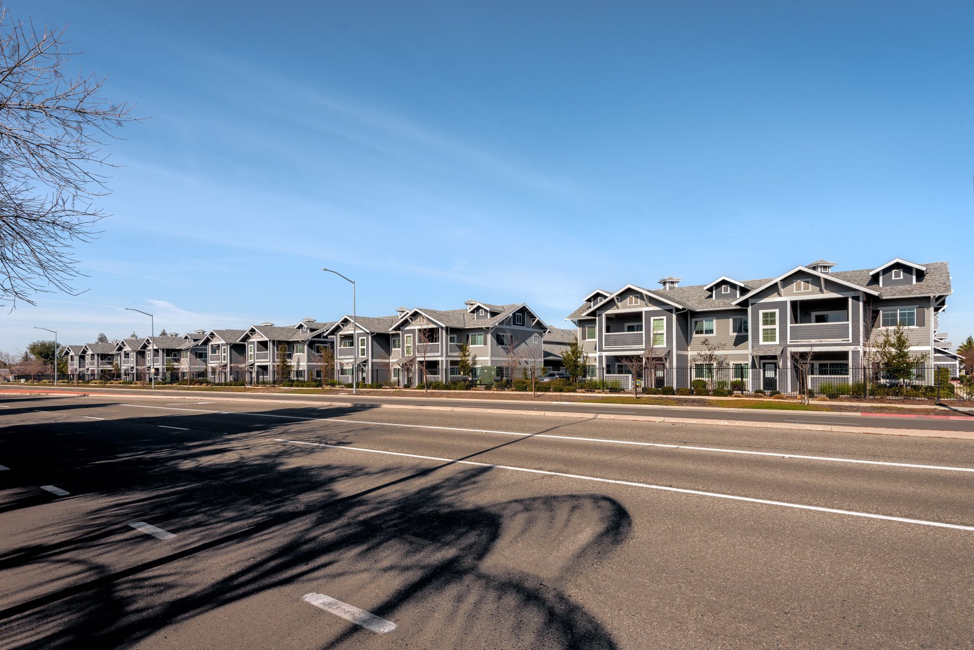 Row of gray multi-story townhouses along a road under a clear, blue sky.