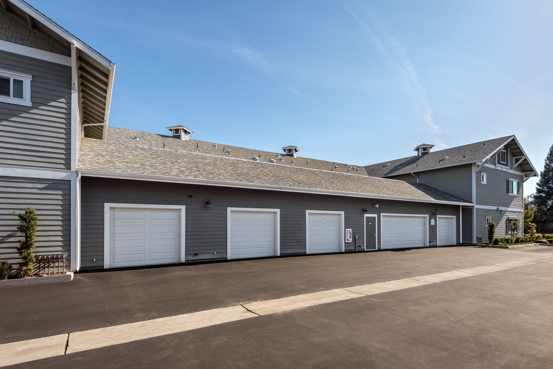 Gray building with multiple white garage doors; clear blue sky.