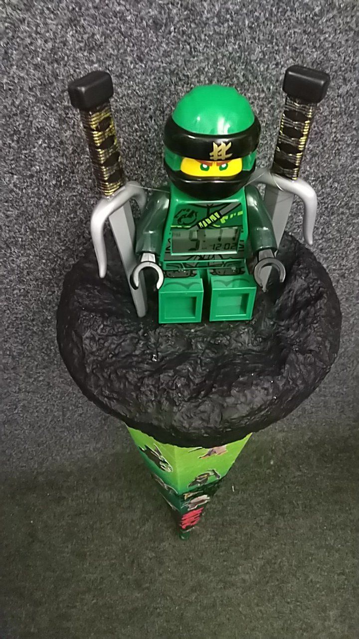 Eine grüne Lego-Ninjago-Figur sitzt auf einem schwarzen Kegel.