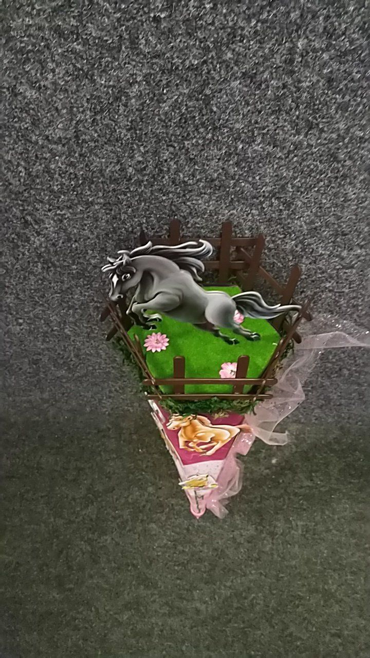 Auf einem grünen Zaun sitzt ein Spielzeugpferd.