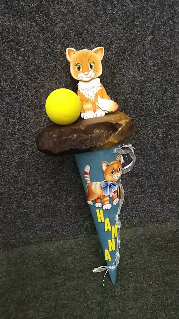 Eine Katze sitzt auf einem Kegel mit einem gelben Ball.