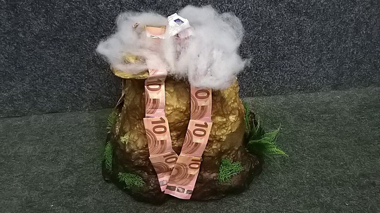 Auf einem Tisch steht ein Vulkan aus Geld.