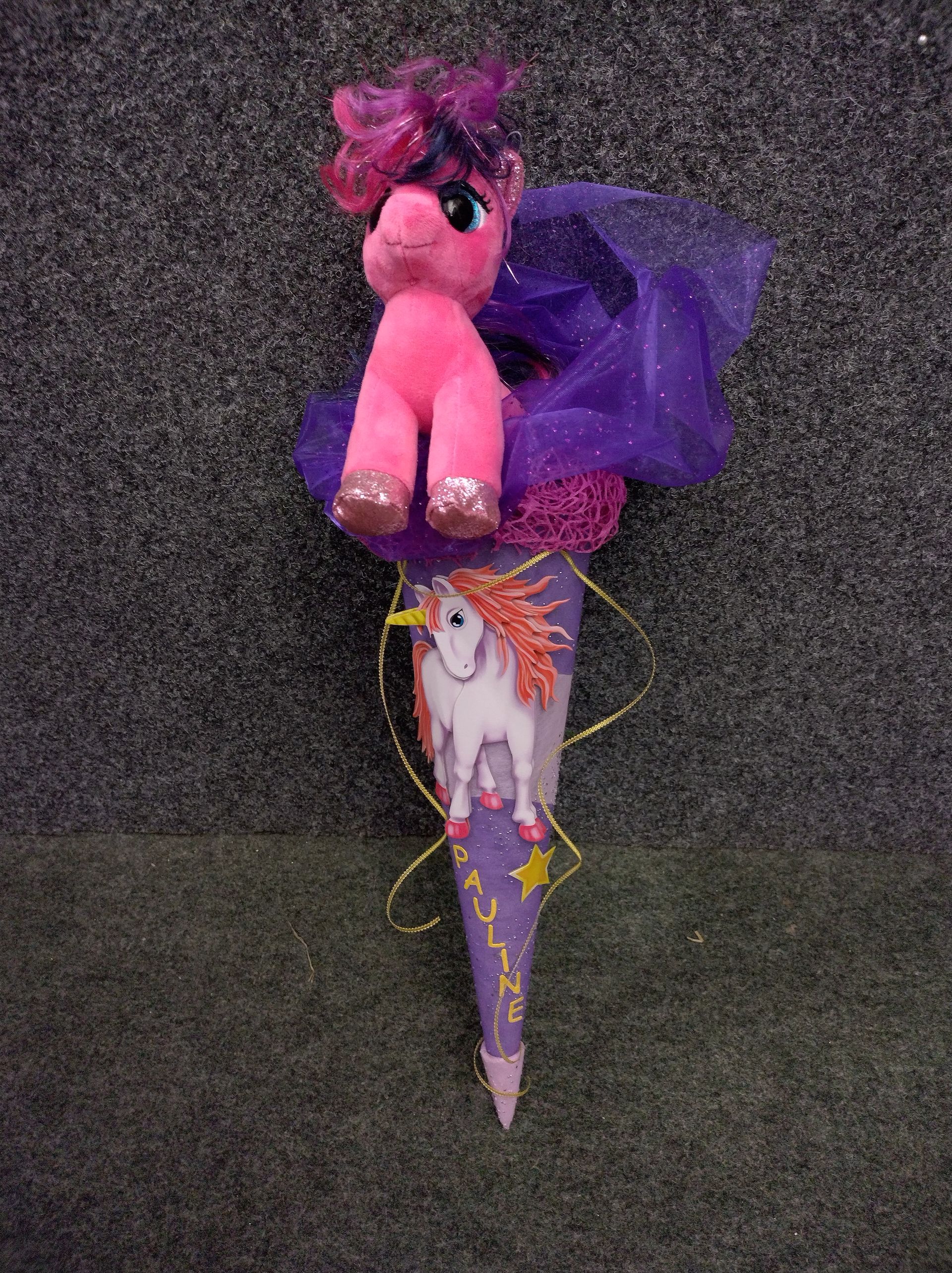 Ein ausgestopftes rosa Einhorn sitzt auf einem lila Kegel.