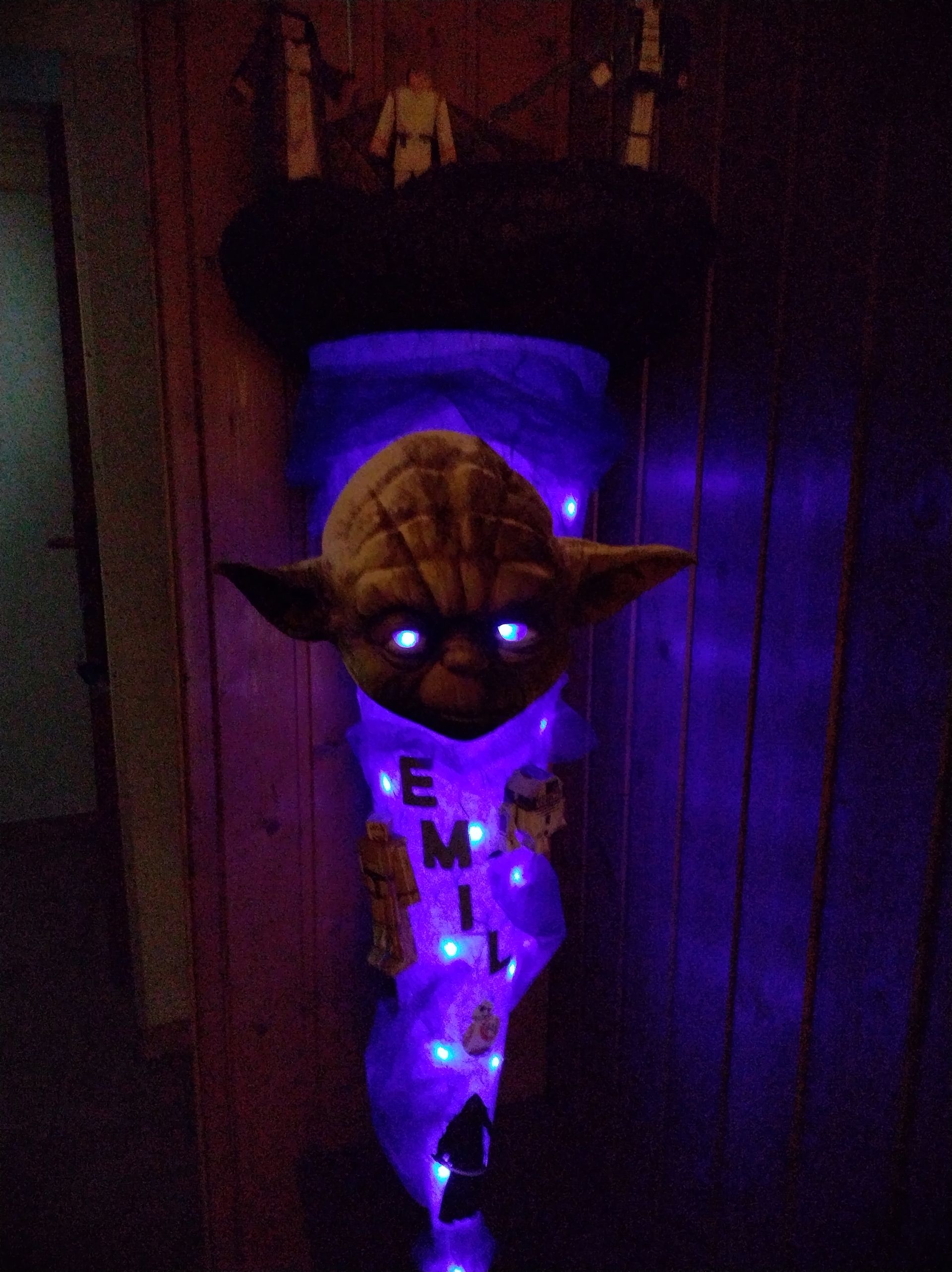 An einer Wand hängt ein Yoda-Weihnachtsstrumpf mit Lichtern.