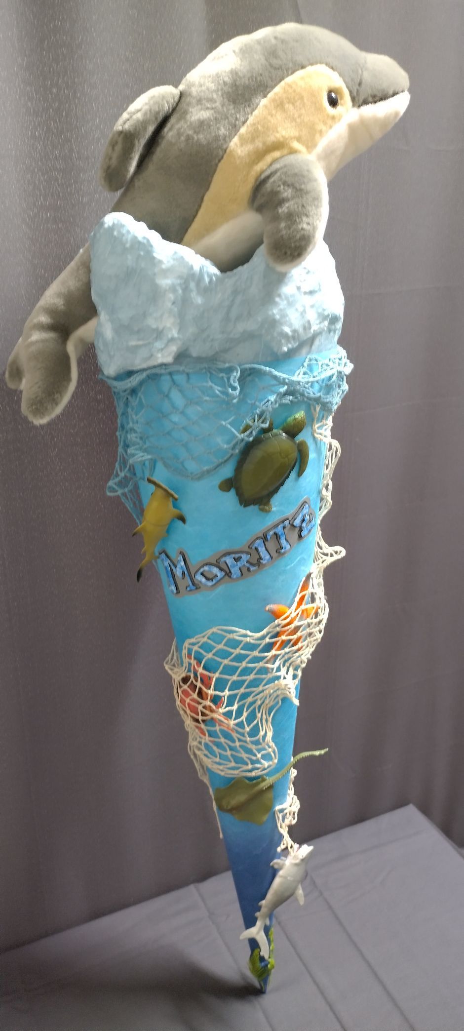 Auf einem blauen Kegel sitzt ein ausgestopfter Delphin.