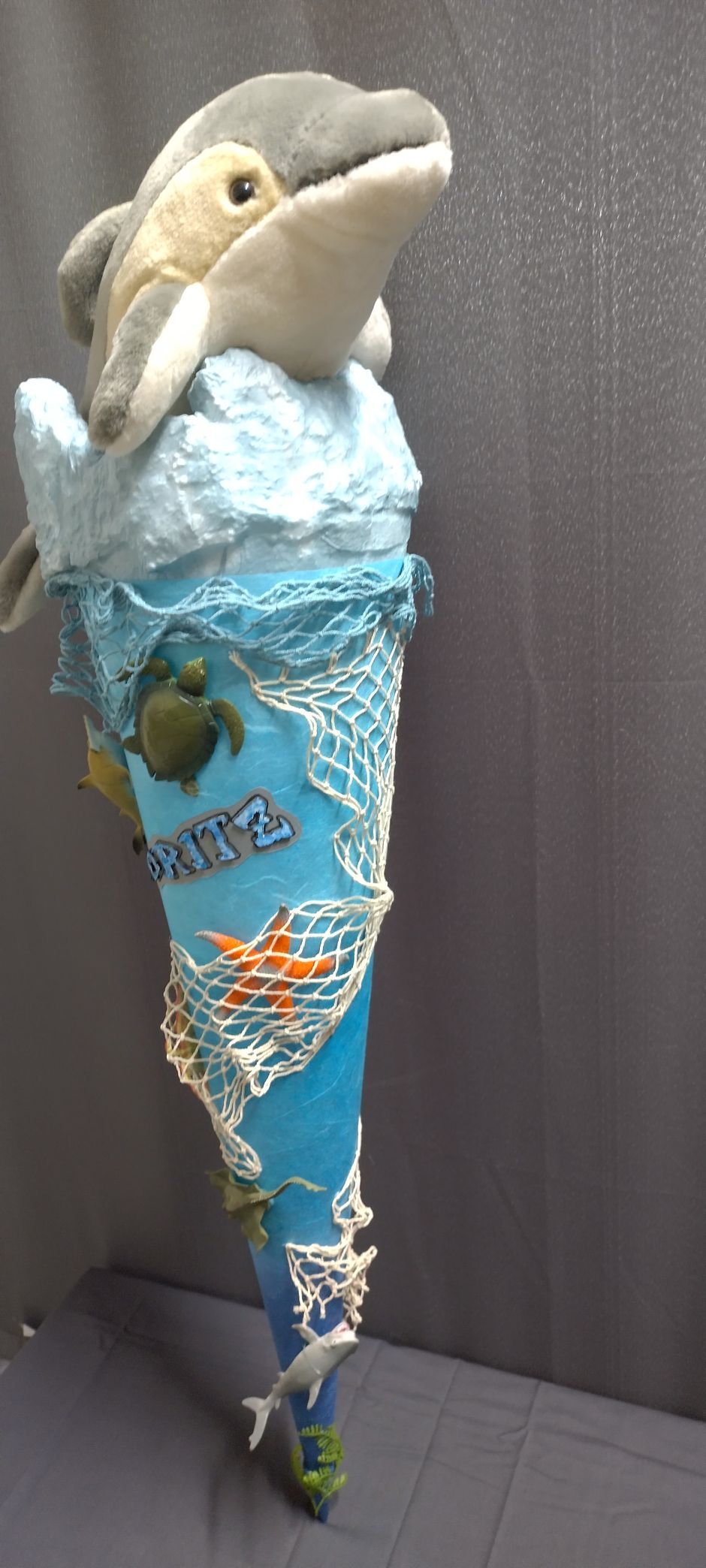 Auf einem blauen Kegel sitzt ein ausgestopfter Delphin.