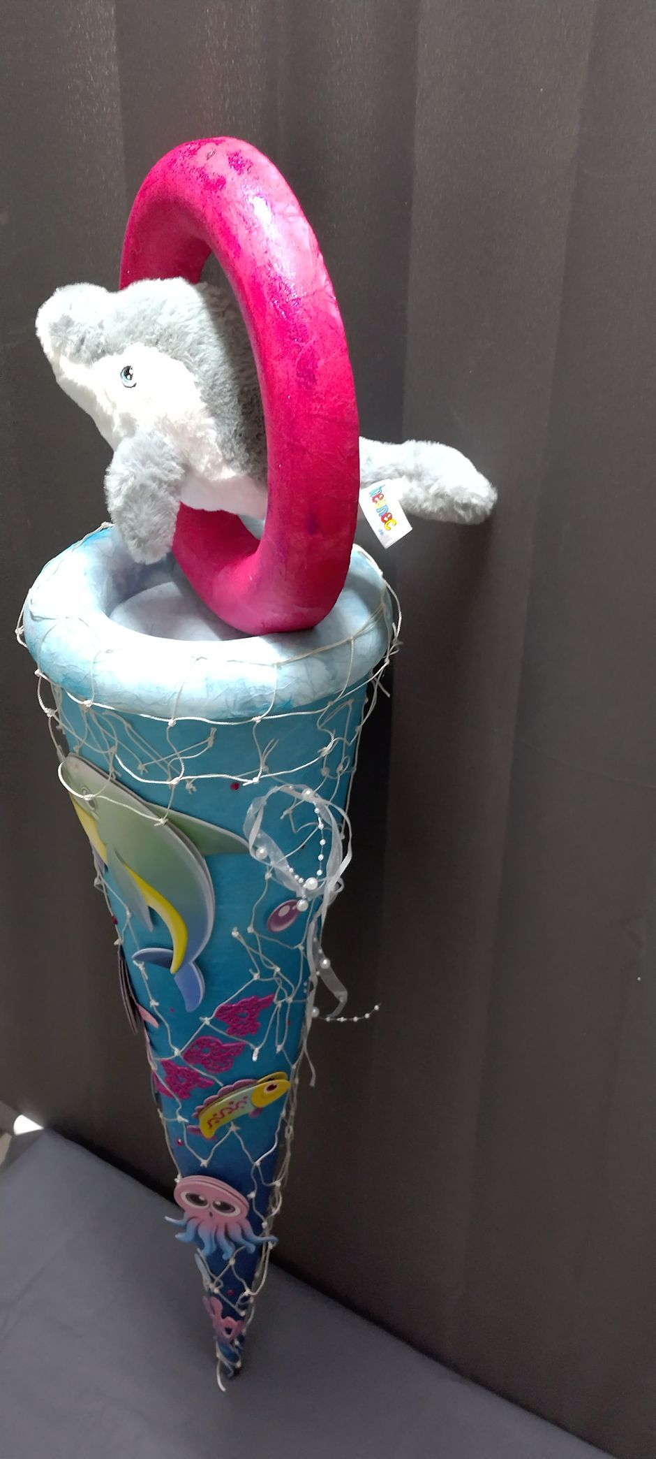 Auf einem blauen Kegel sitzt ein ausgestopfter Delphin.