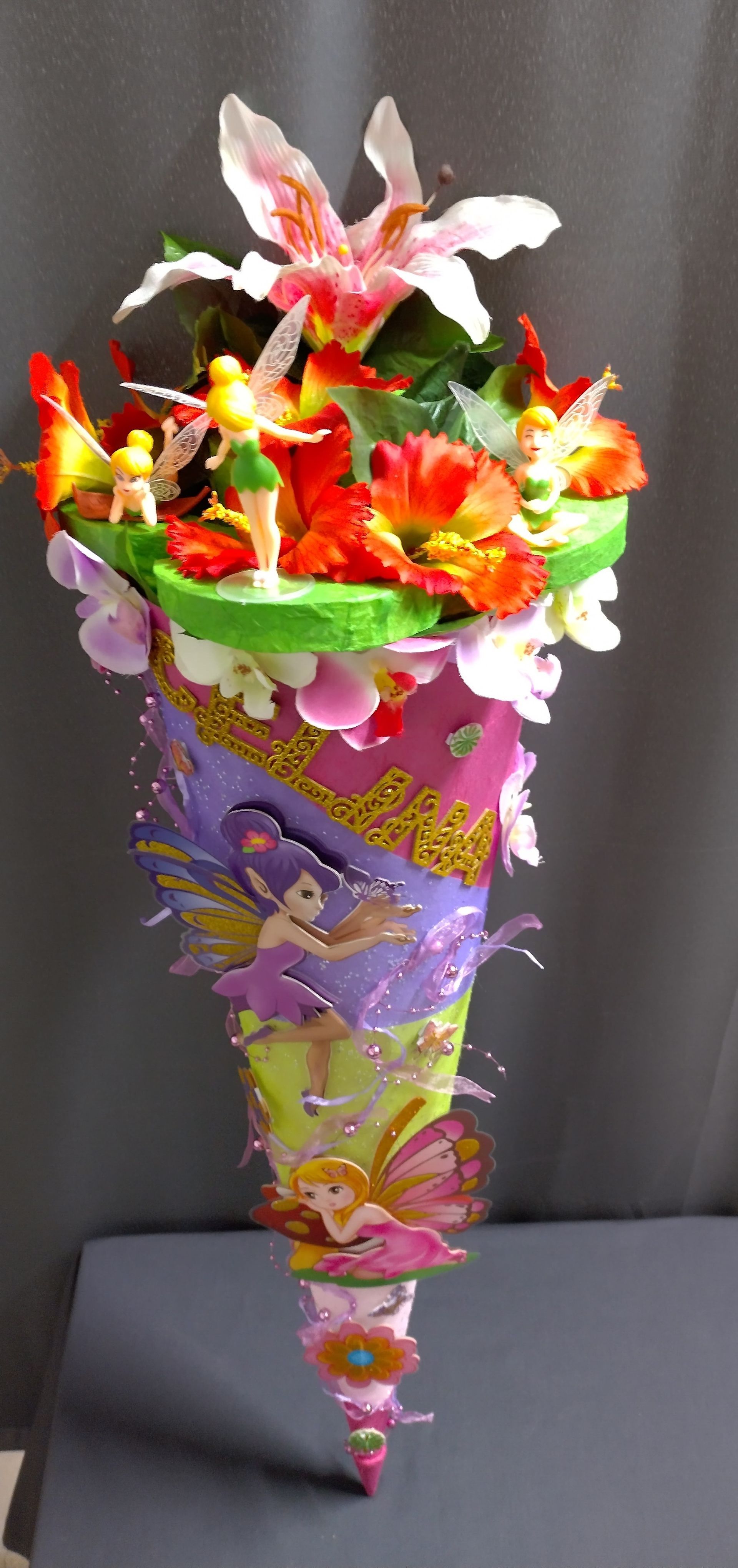 Auf einem Tisch steht ein mit Blumen und Feen gefüllter Kegel.