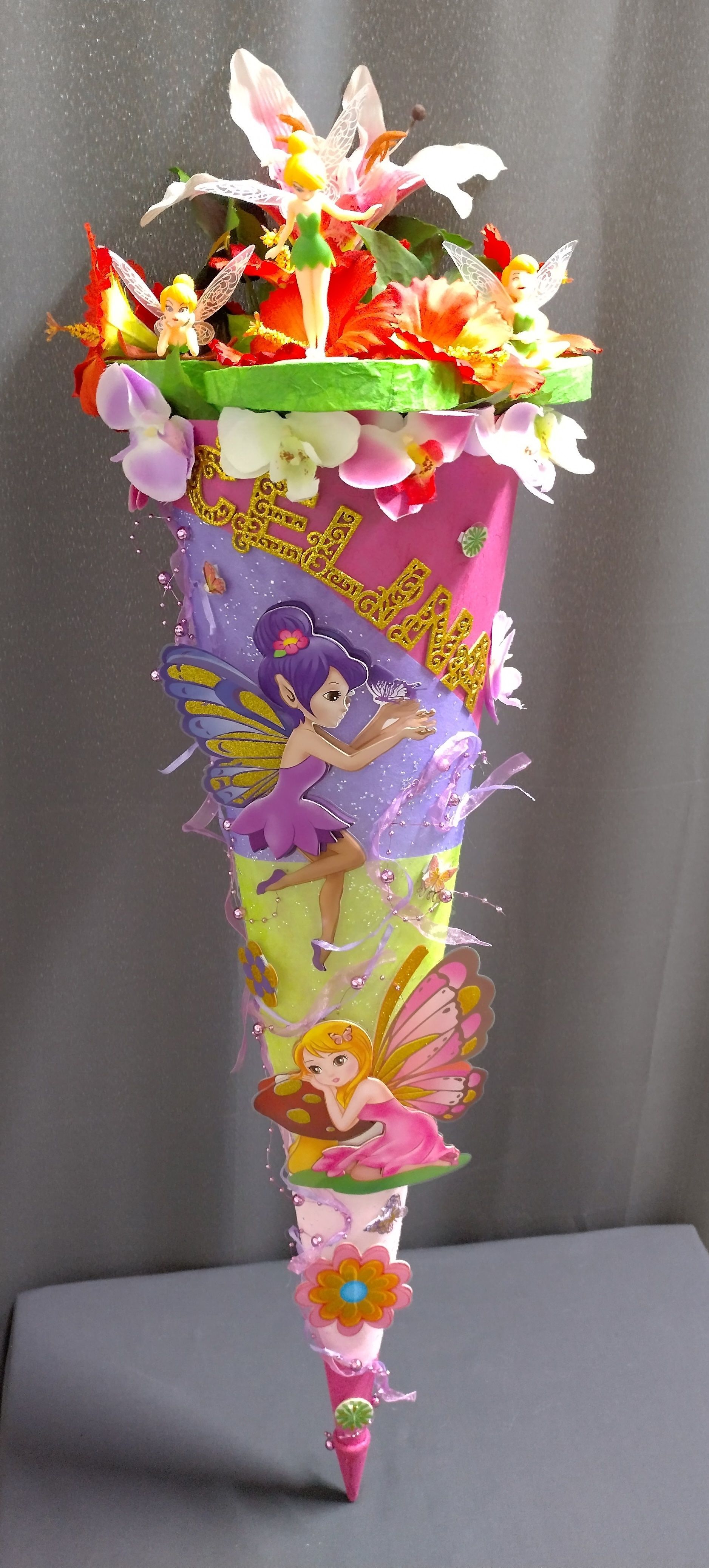 Auf einem Tisch steht ein Kegel mit Blumen und Feen darauf.