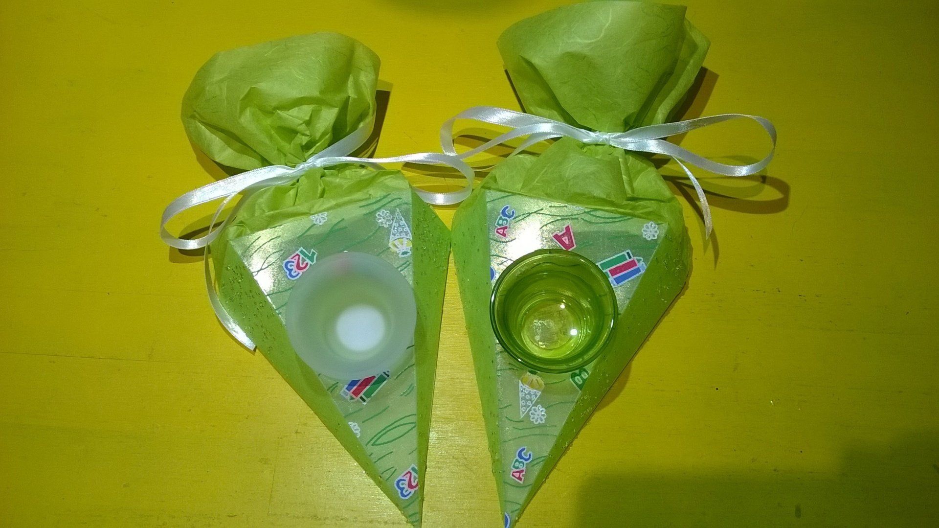 Zwei grüne Taschen mit einer Kerze darin auf einem gelben Tisch.