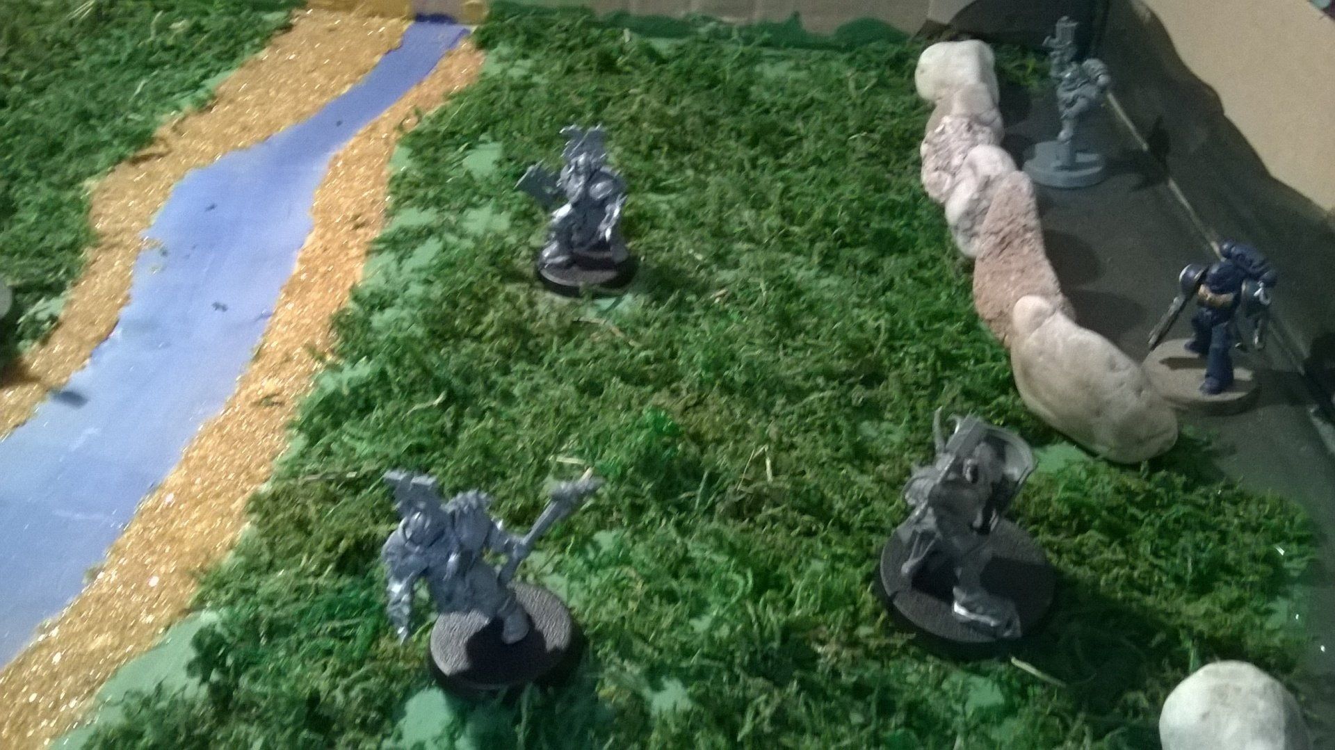 Eine Gruppe von Figuren sitzt auf einer Wiese neben einem Fluss.